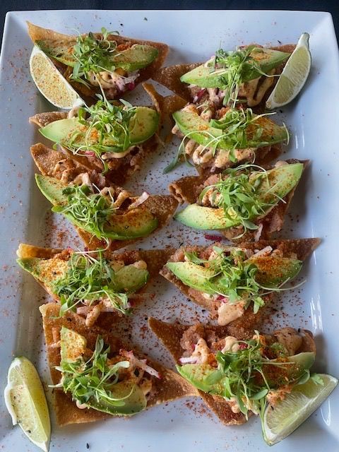 Plated tacos topped with greens and sauce, garnished with lime wedges on a white platter