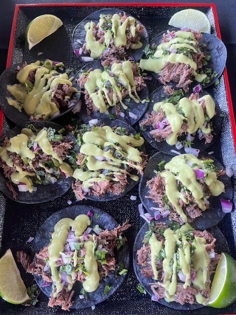 Black tray of nacho-style chips topped with guacamole and red onions, garnished with lime wedges