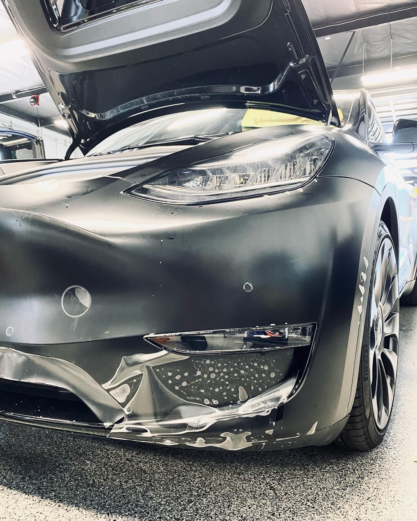 Black Tesla with opened doors, front bumper peeling, in a bright garage.