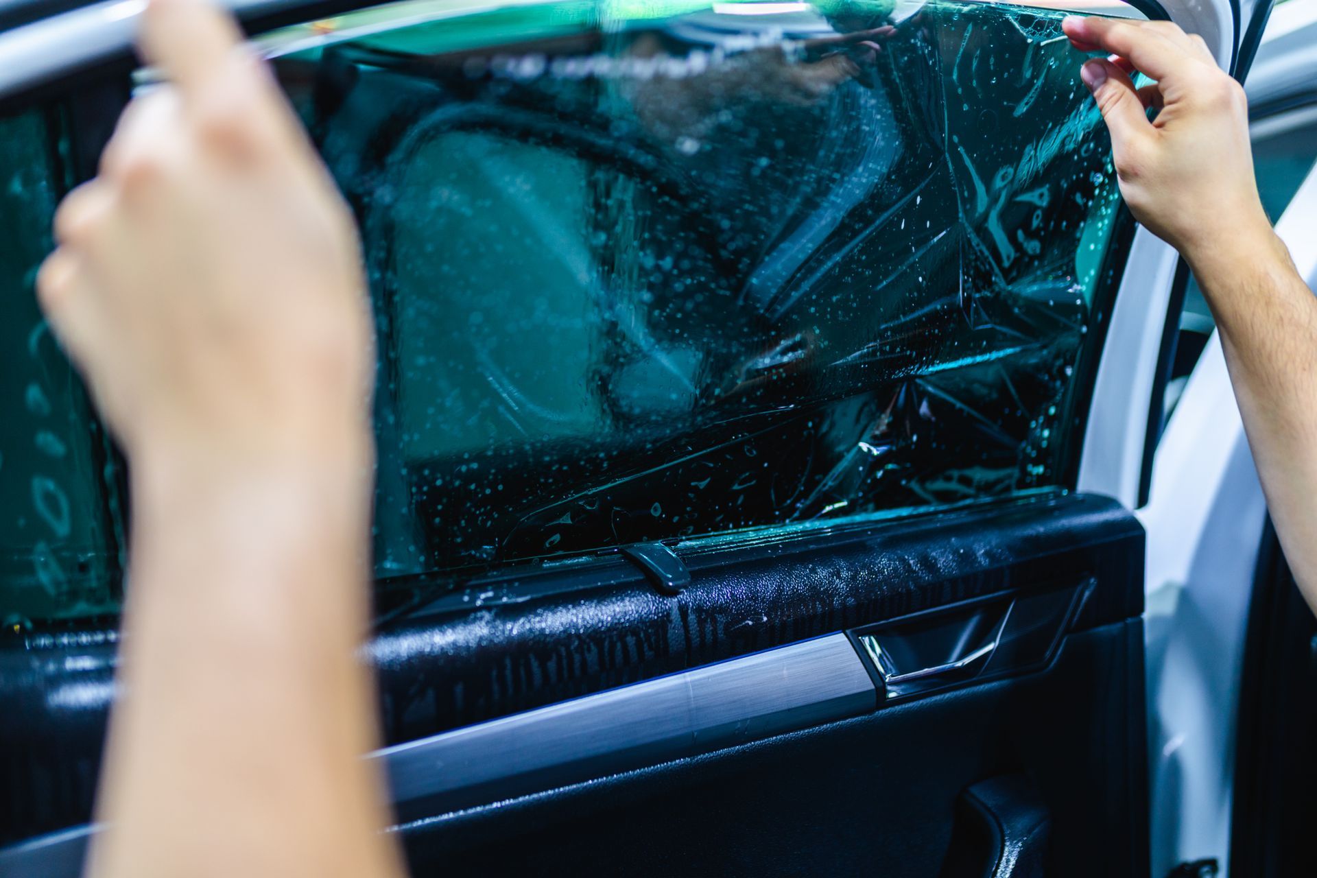 Person applying tinted film to a car window.