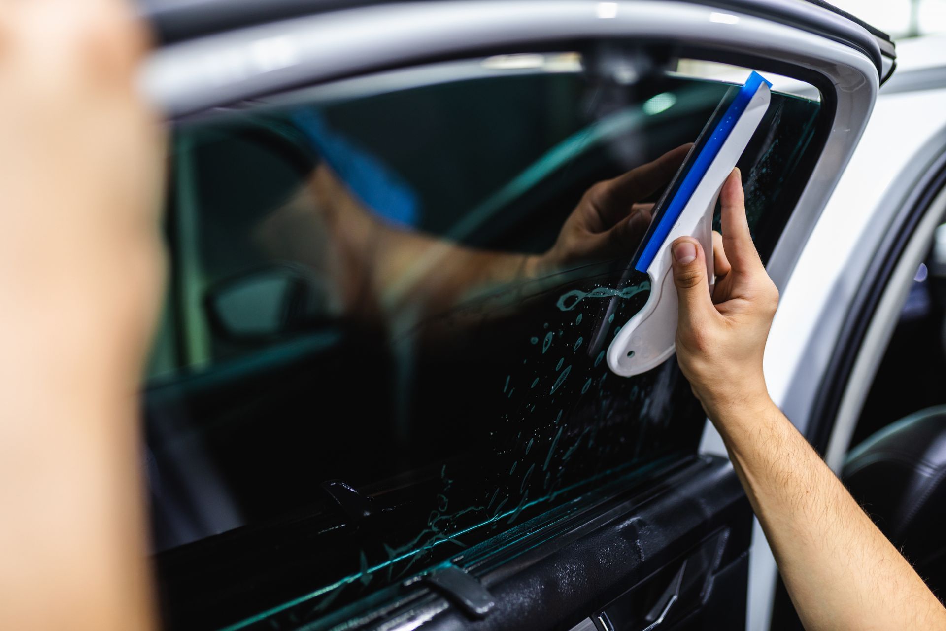 A person is applying tinted window film to a car window.