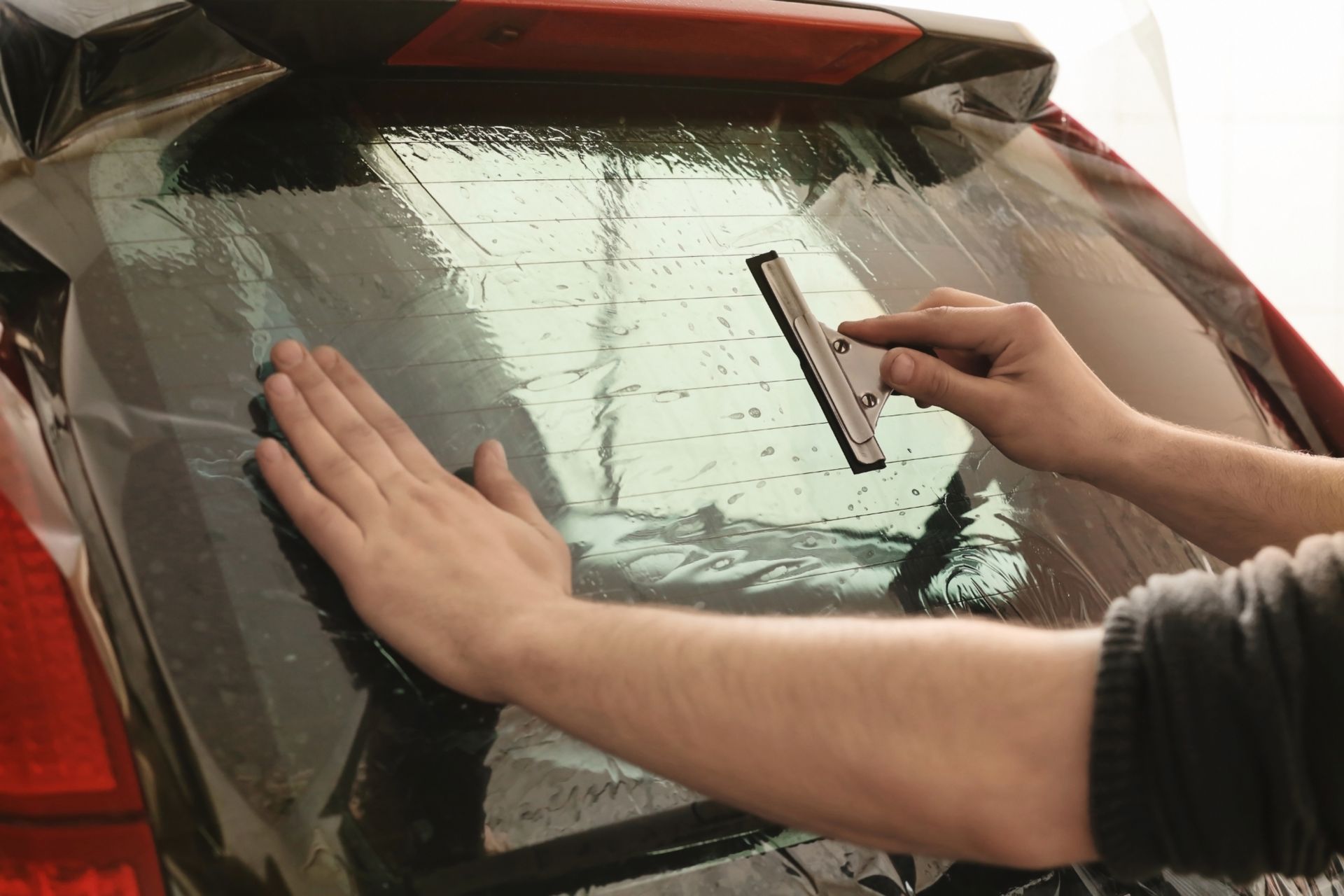 A person is applying tinted glass to the back window of a car.