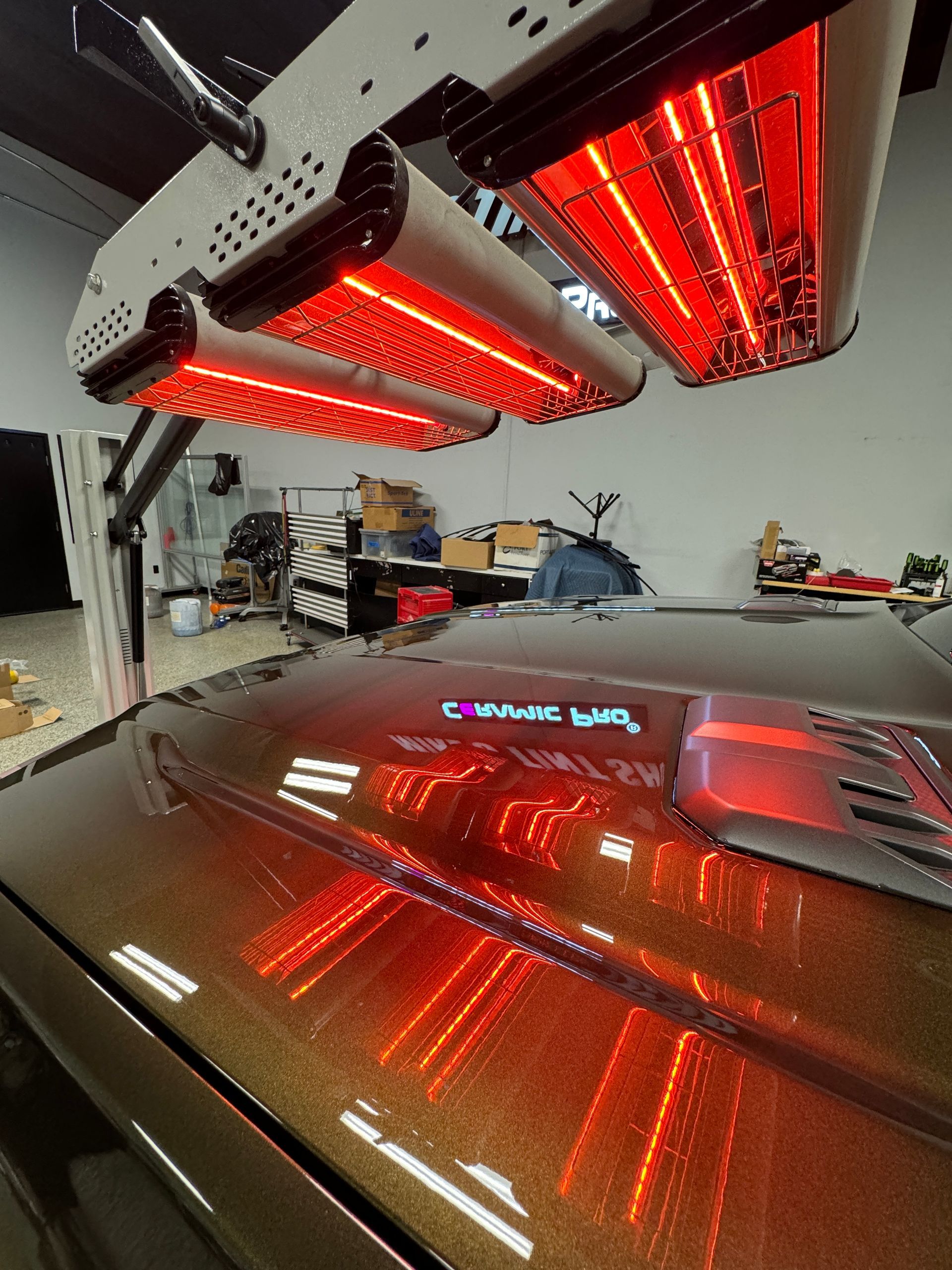 Red infrared heat lamps over a car hood in a garage, reflecting bright red light on the paint.