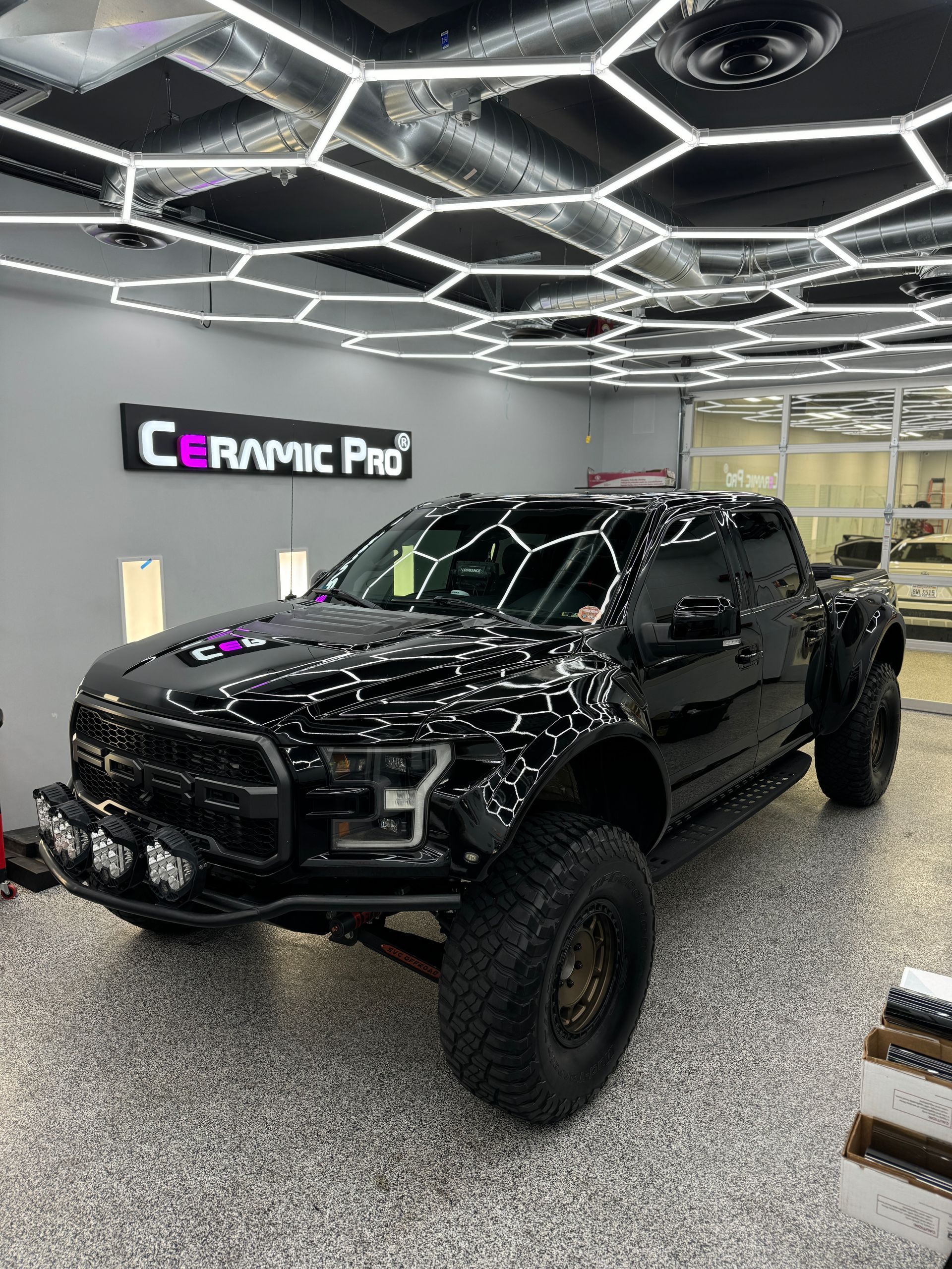 Black lifted truck in a Ceramic Pro showroom under bright hexagonal ceiling lights.