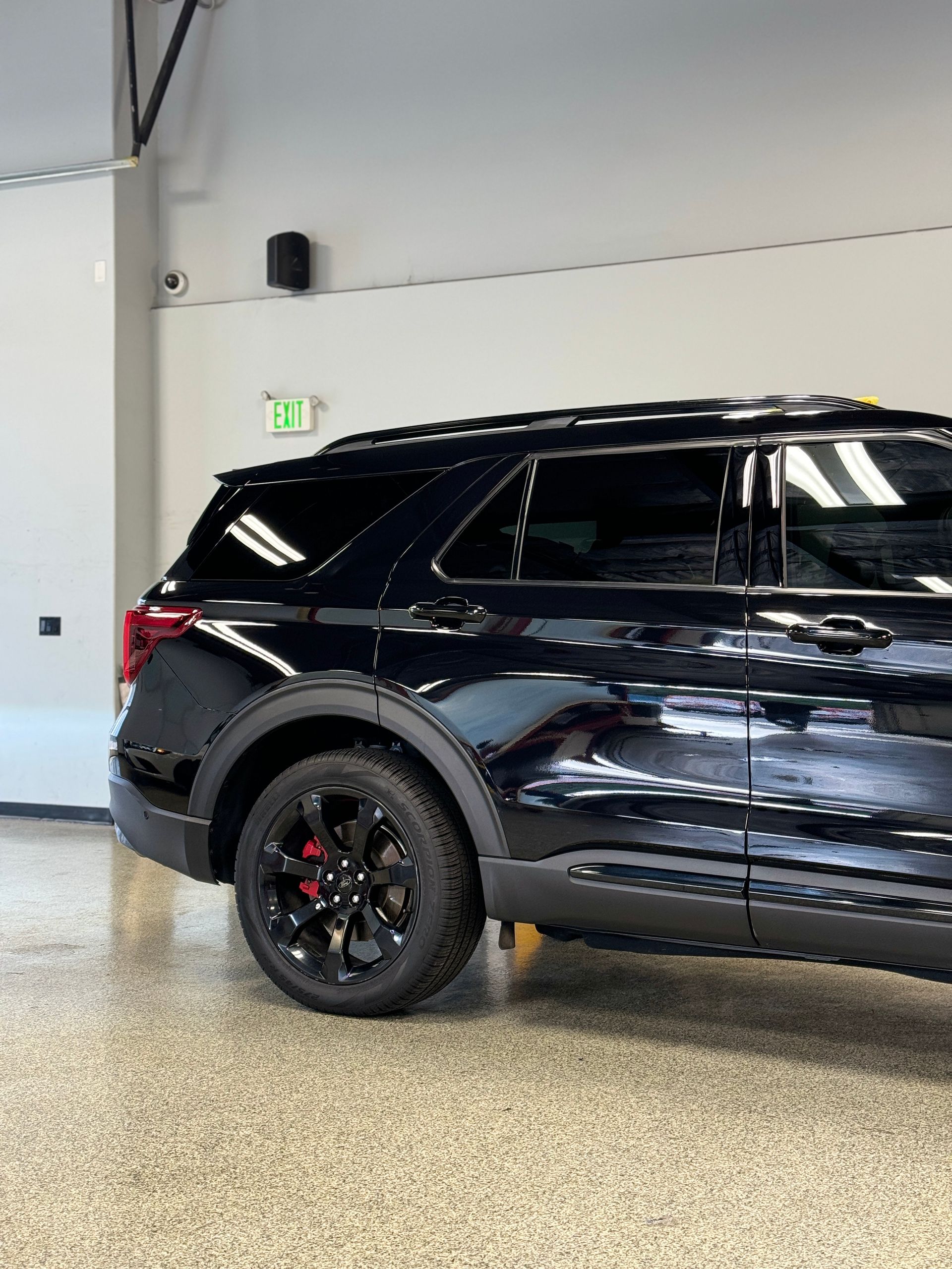 A black suv is parked in a garage with a green exit sign on the wall.