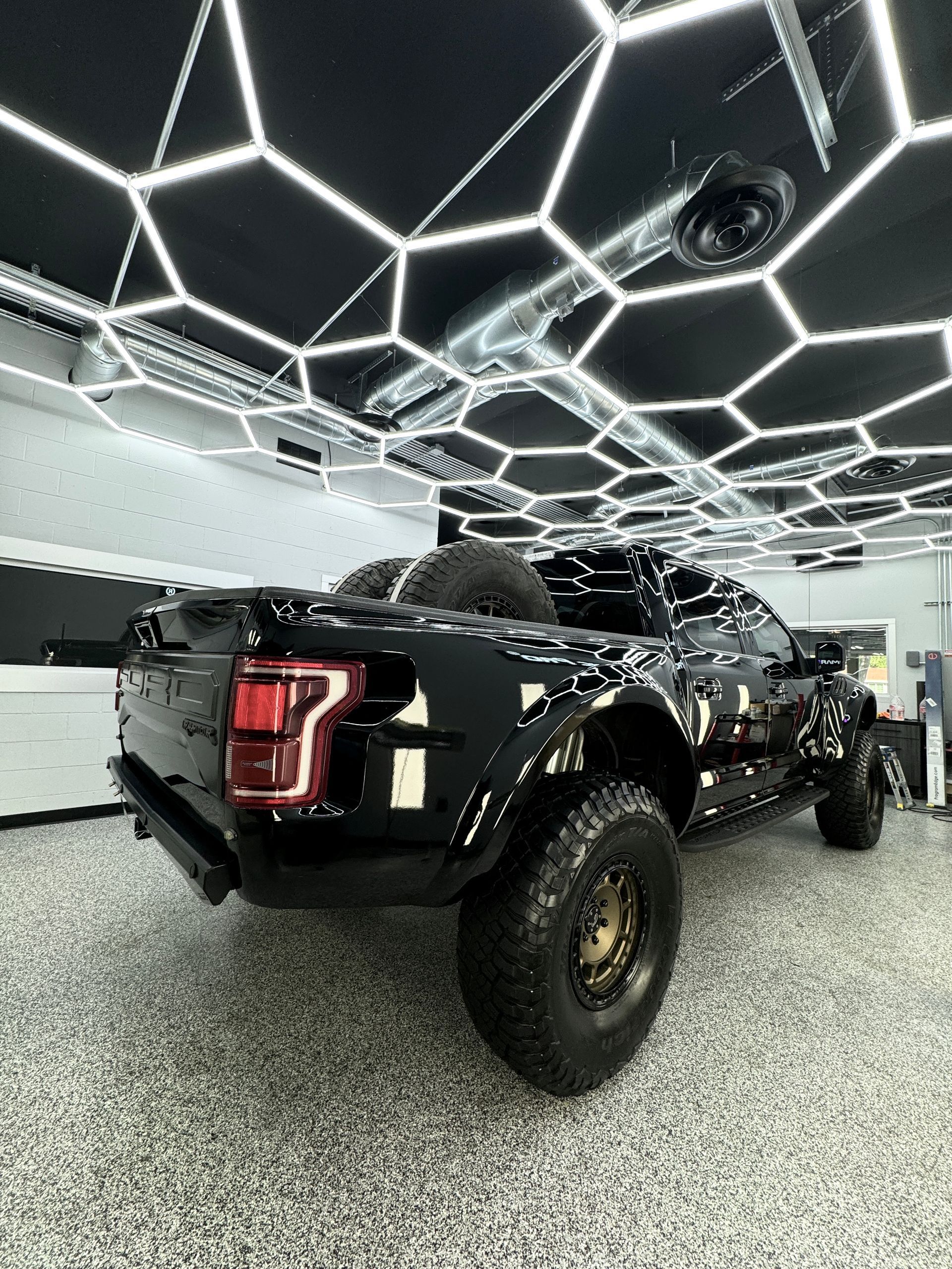 A black truck is parked in a garage with a honeycomb ceiling.