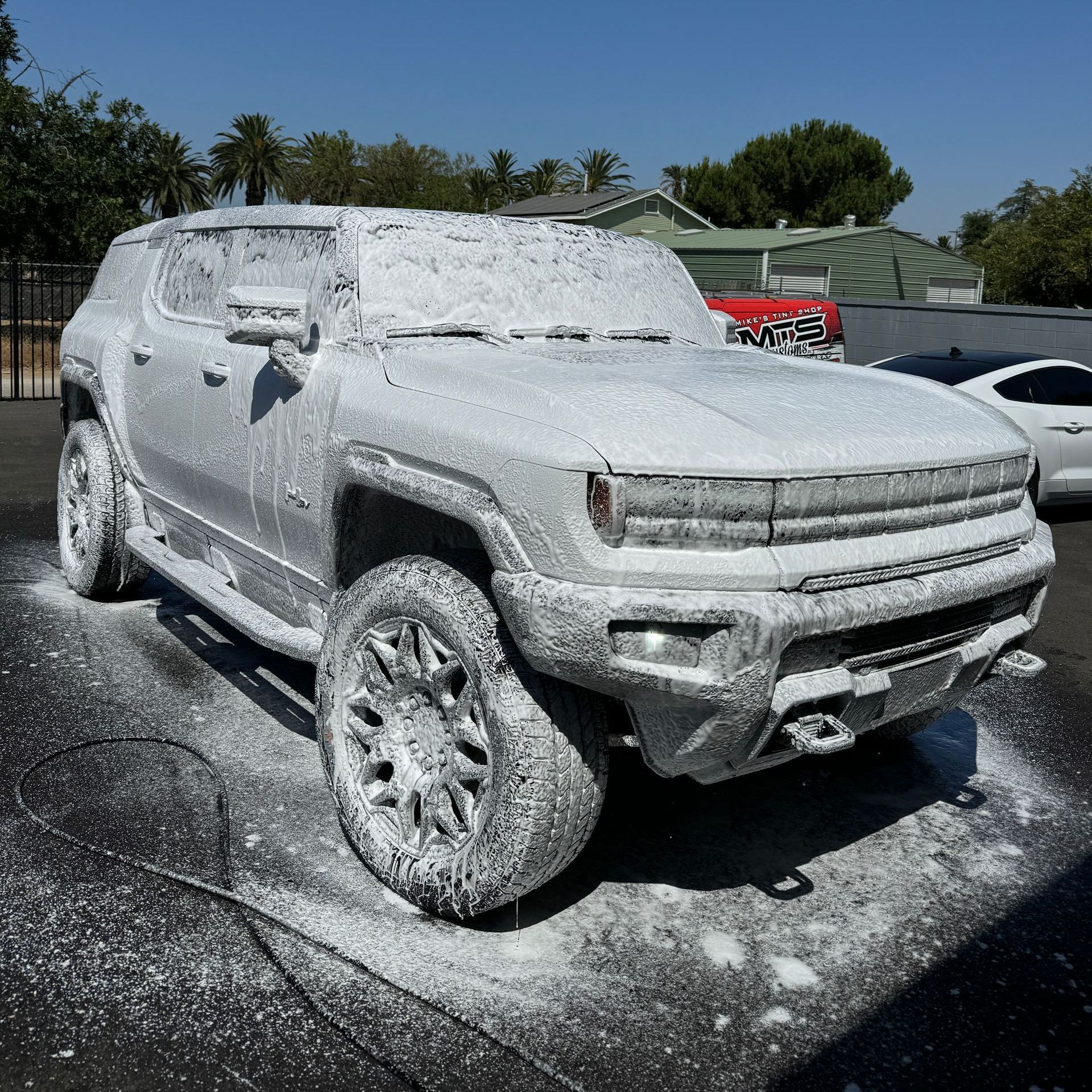 A white suv is covered in foam on a sunny day