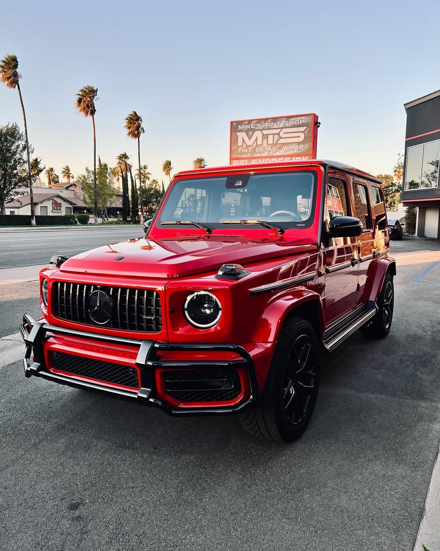 A red mercedes benz g63 is parked on the side of the road.