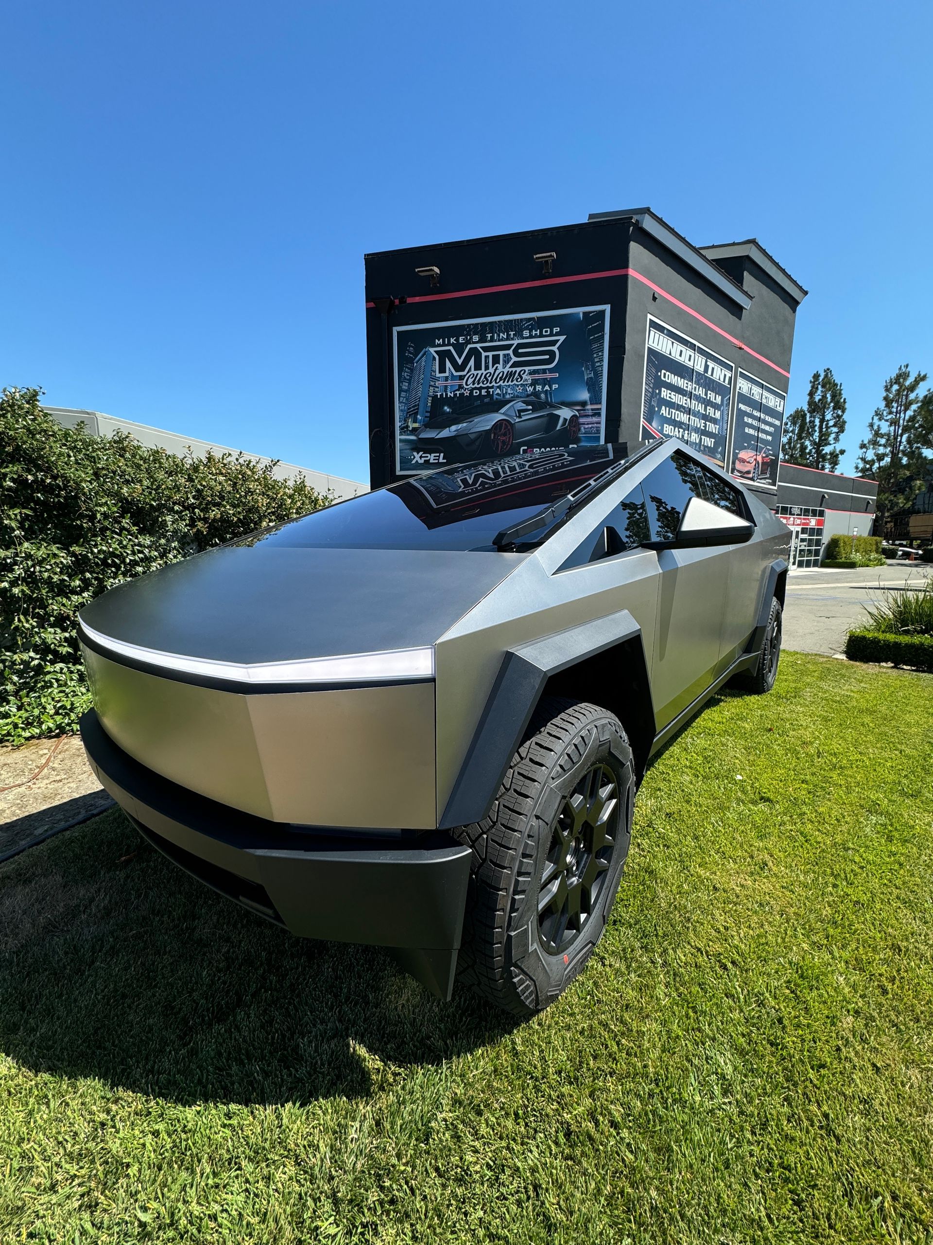 A tesla cybertruck is parked in the grass in front of a building.
