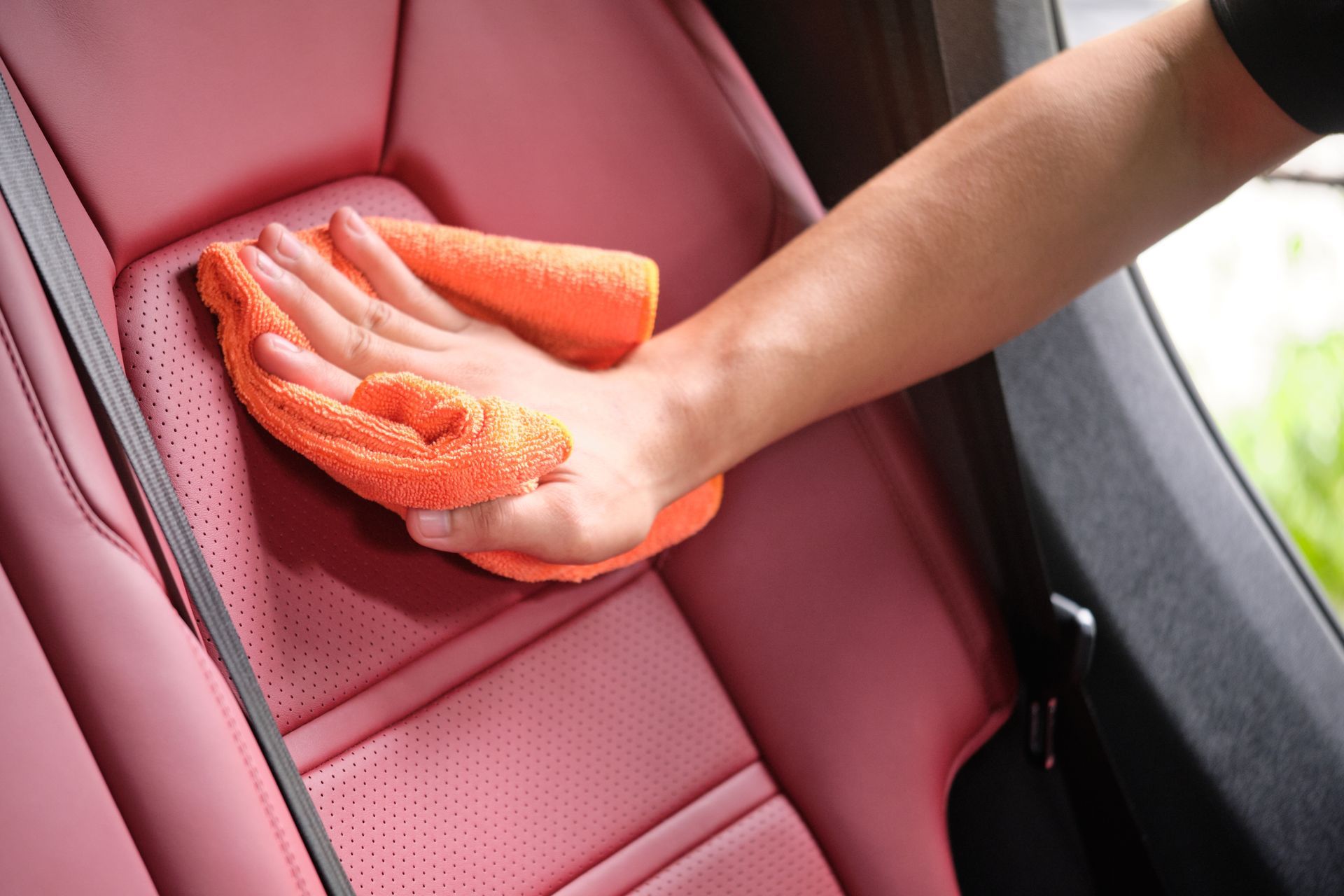 A man is cleaning the back seat of a car with a towel.