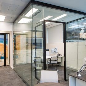 A room with a glass wall and a desk and chairs.