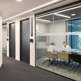 A conference room with a glass wall and people sitting at a table.