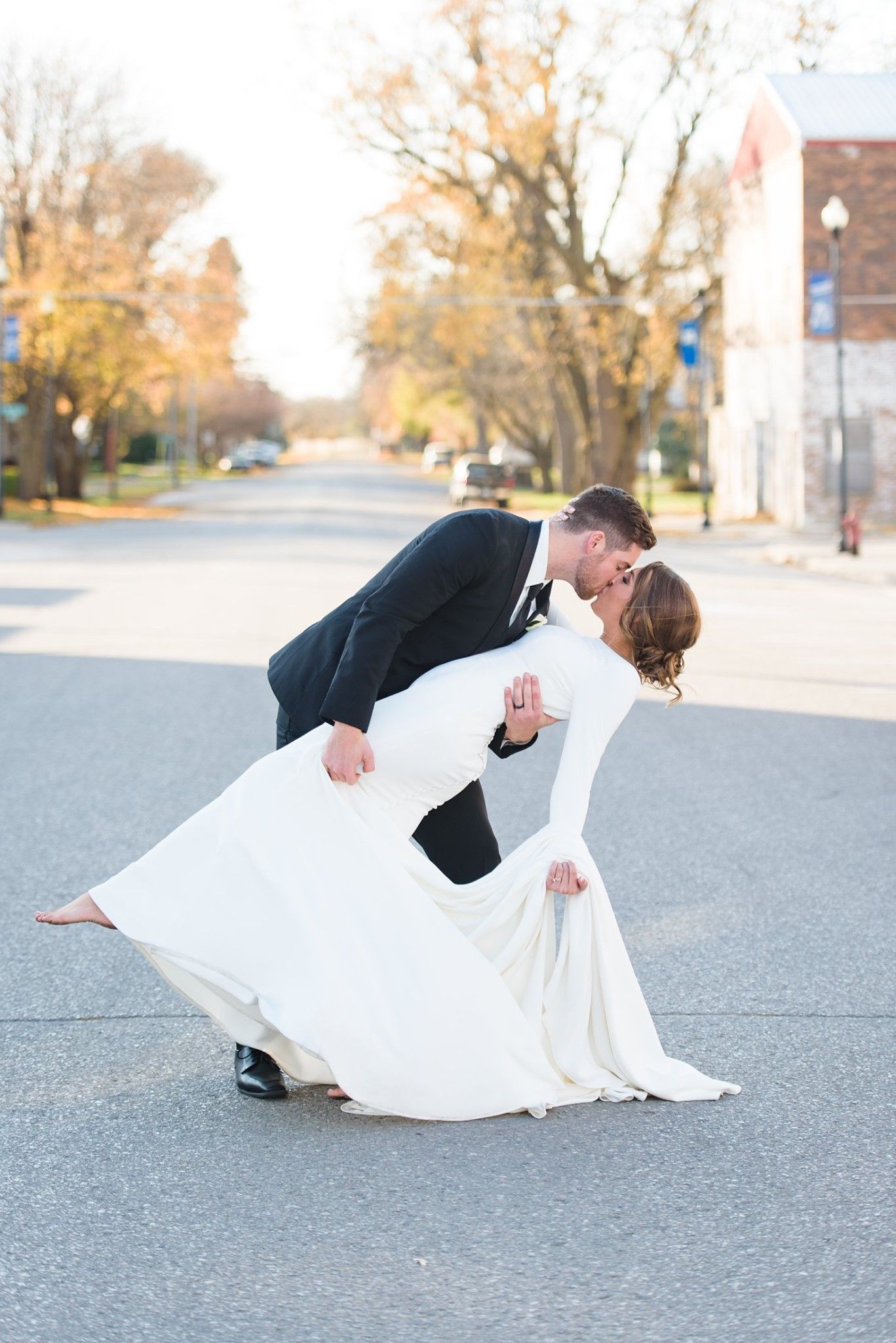 Bride and groom kissing, groom dipping bride on a street, autumn setting.