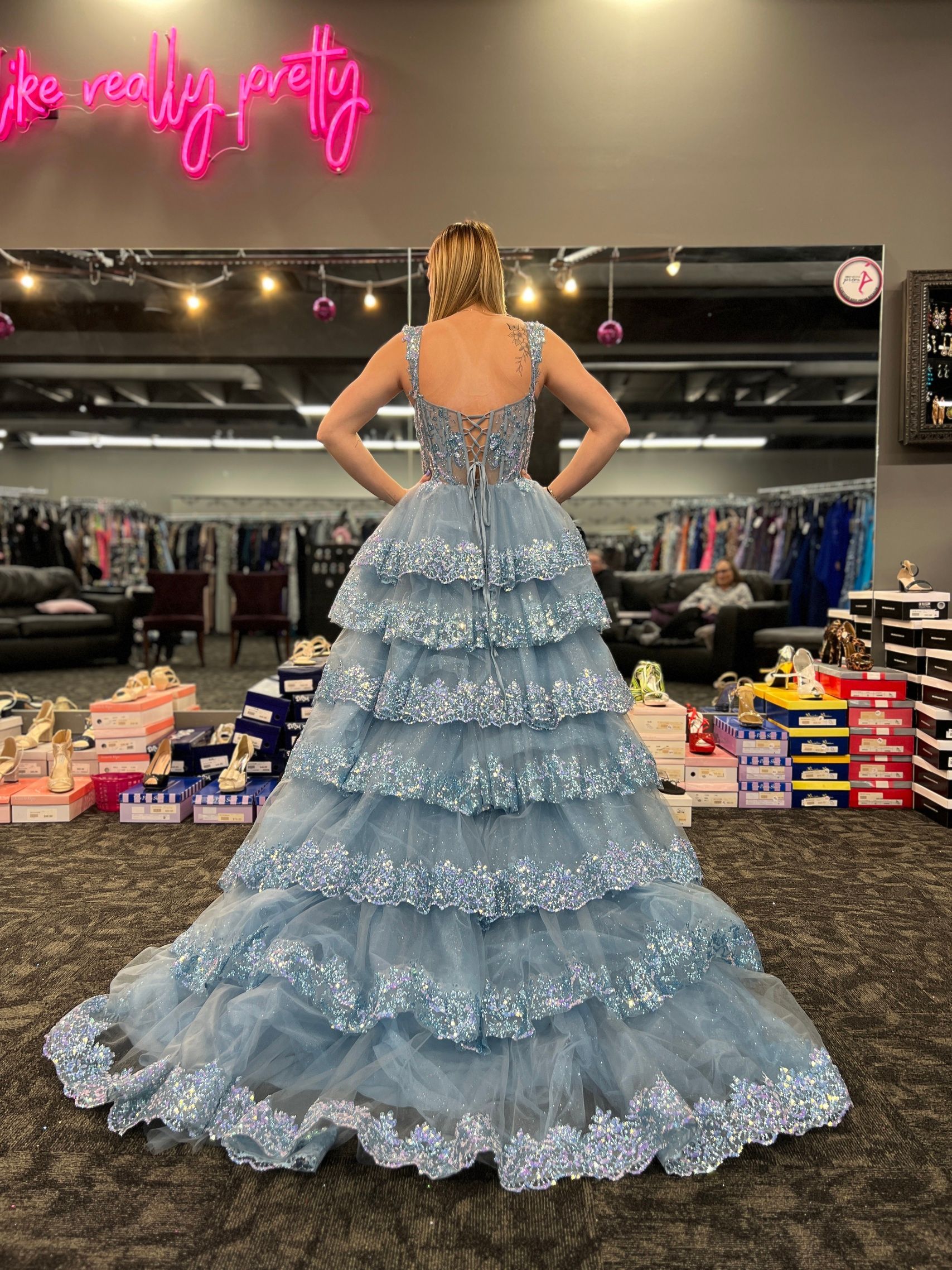 Woman wearing a tiered, sparkly blue gown, standing in a dress shop.