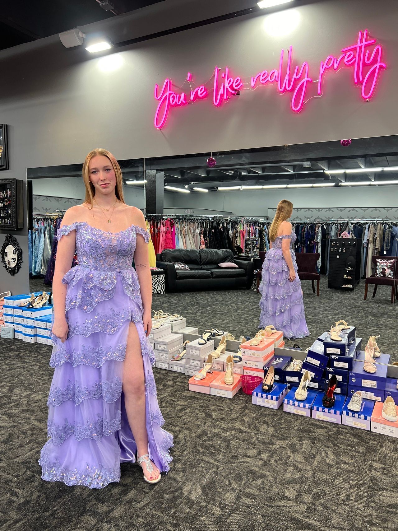 Woman in a lavender off-the-shoulder gown, posing in a dress shop. 