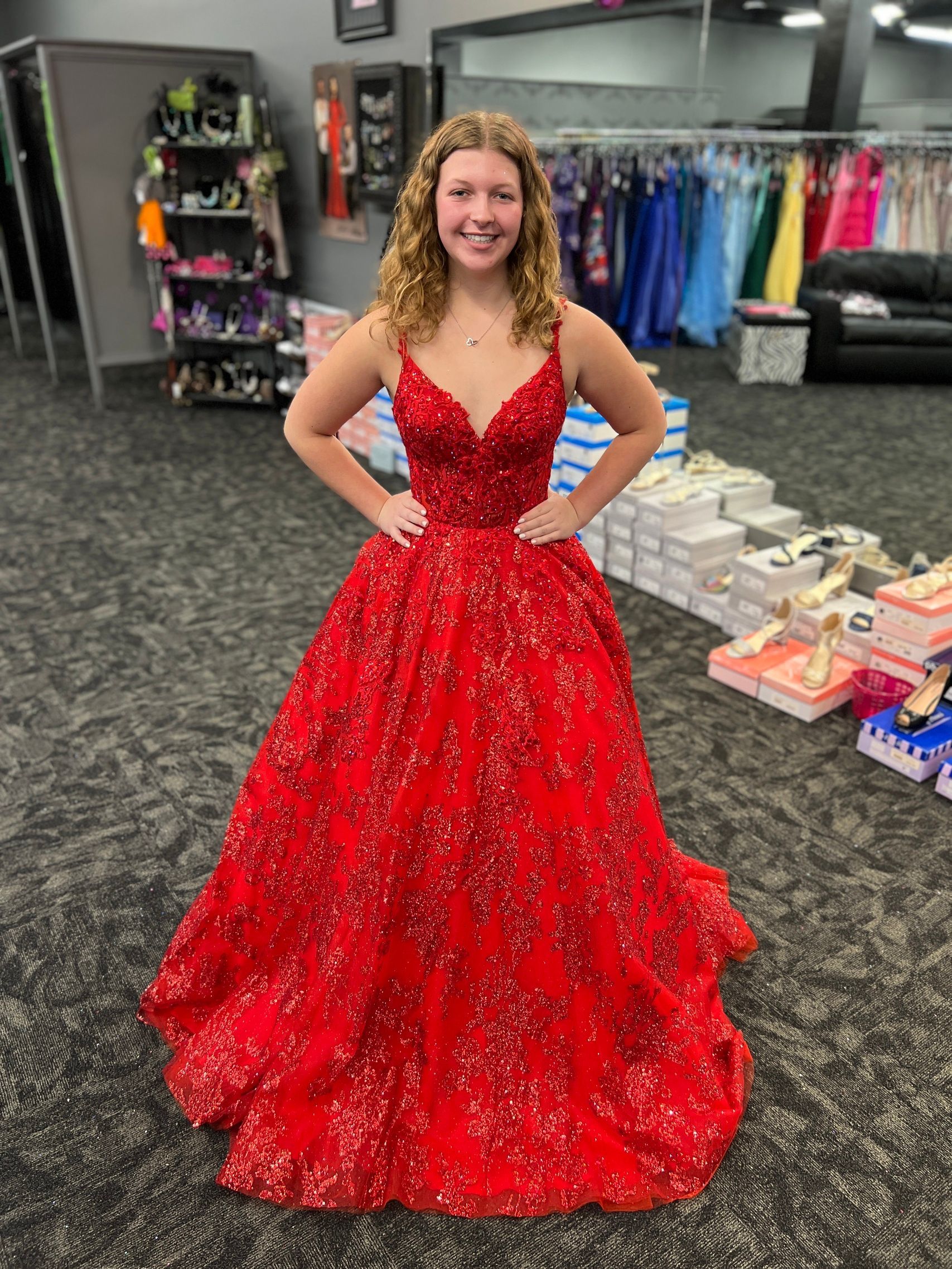 Woman in a sparkly red formal gown with hands on hips, standing in a dress shop.