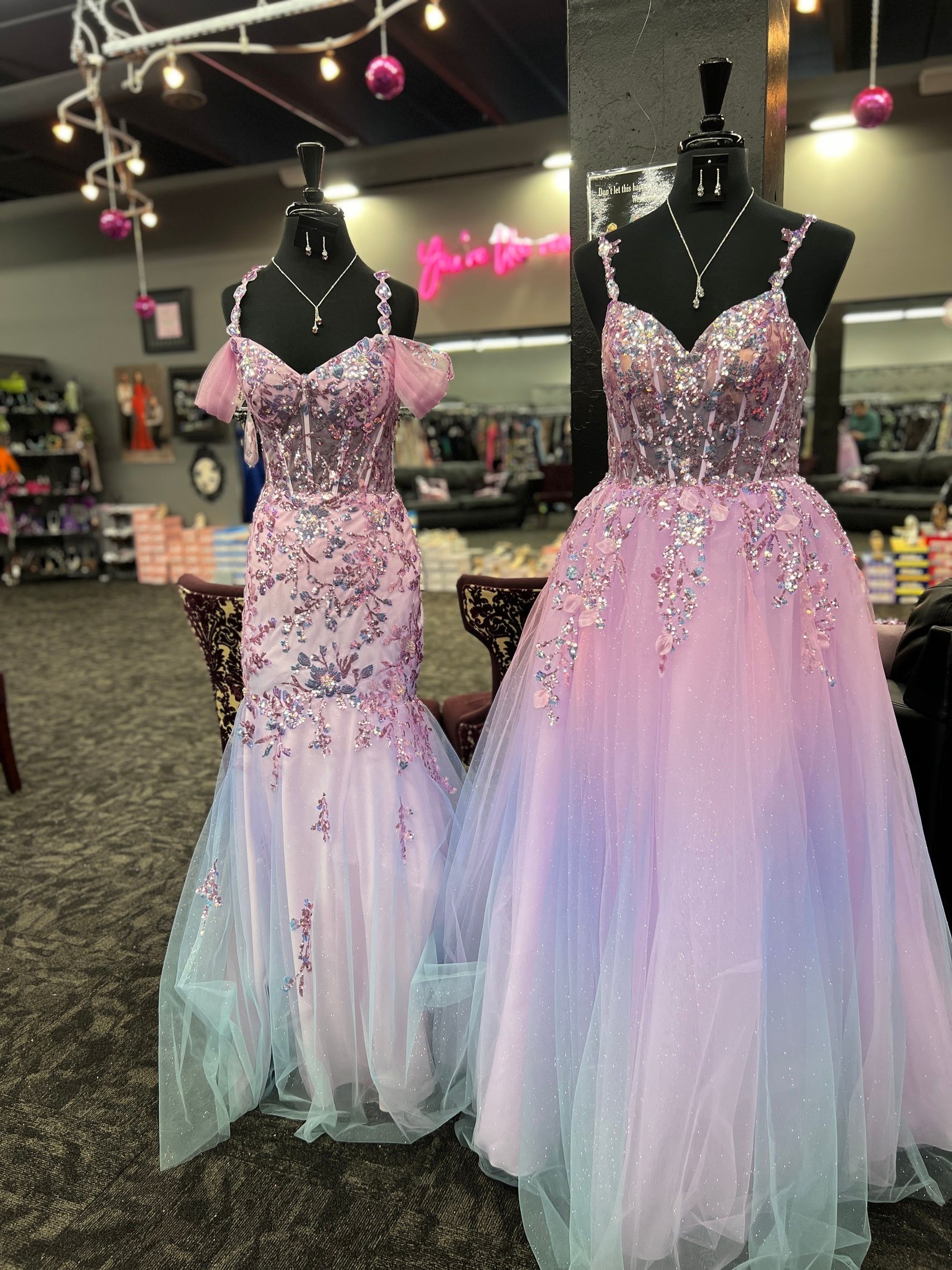 Two pastel prom dresses on mannequins in a store. One is mermaid style, the other a ballgown.