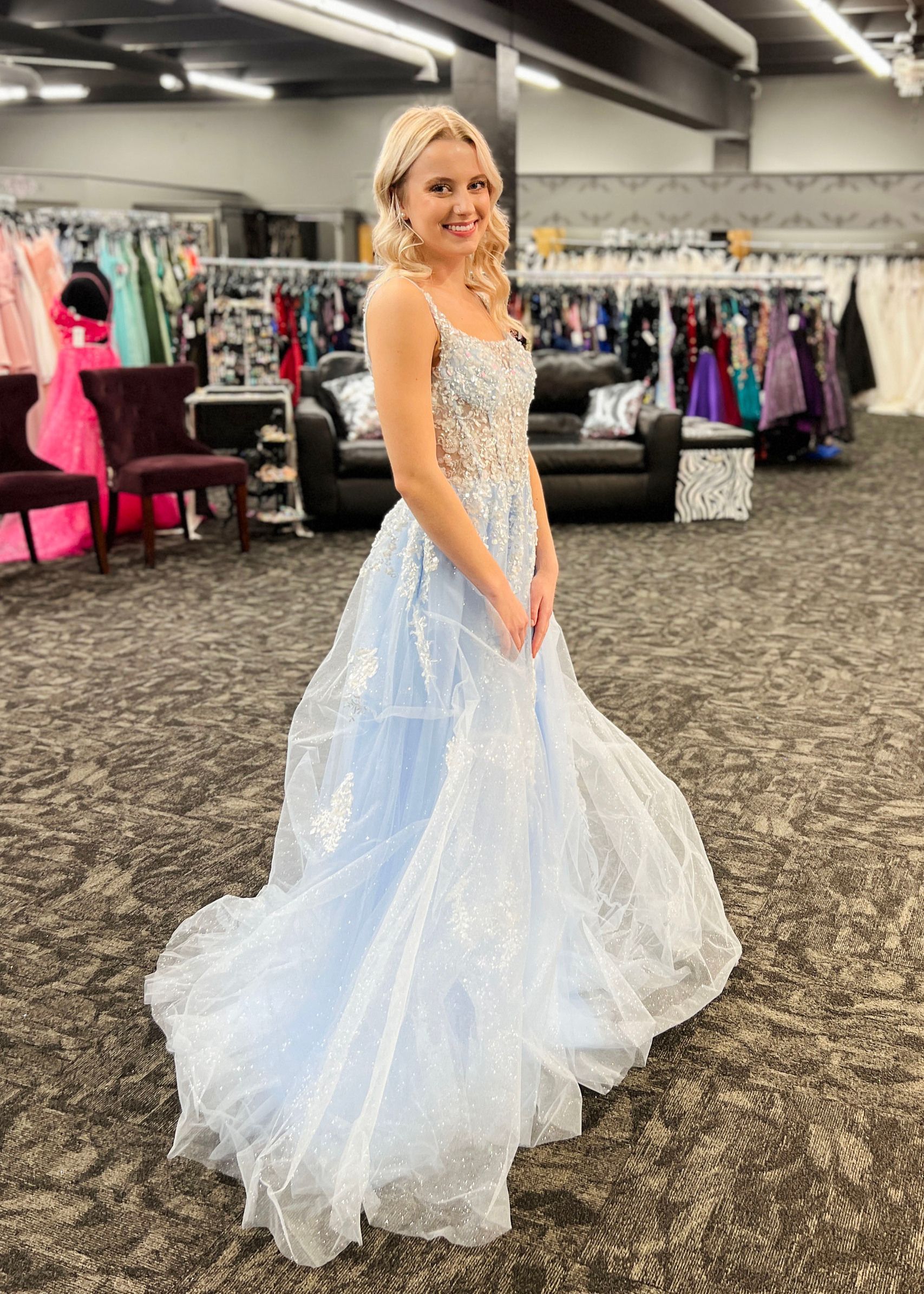Woman in a sparkling light blue gown poses in a formal wear shop.