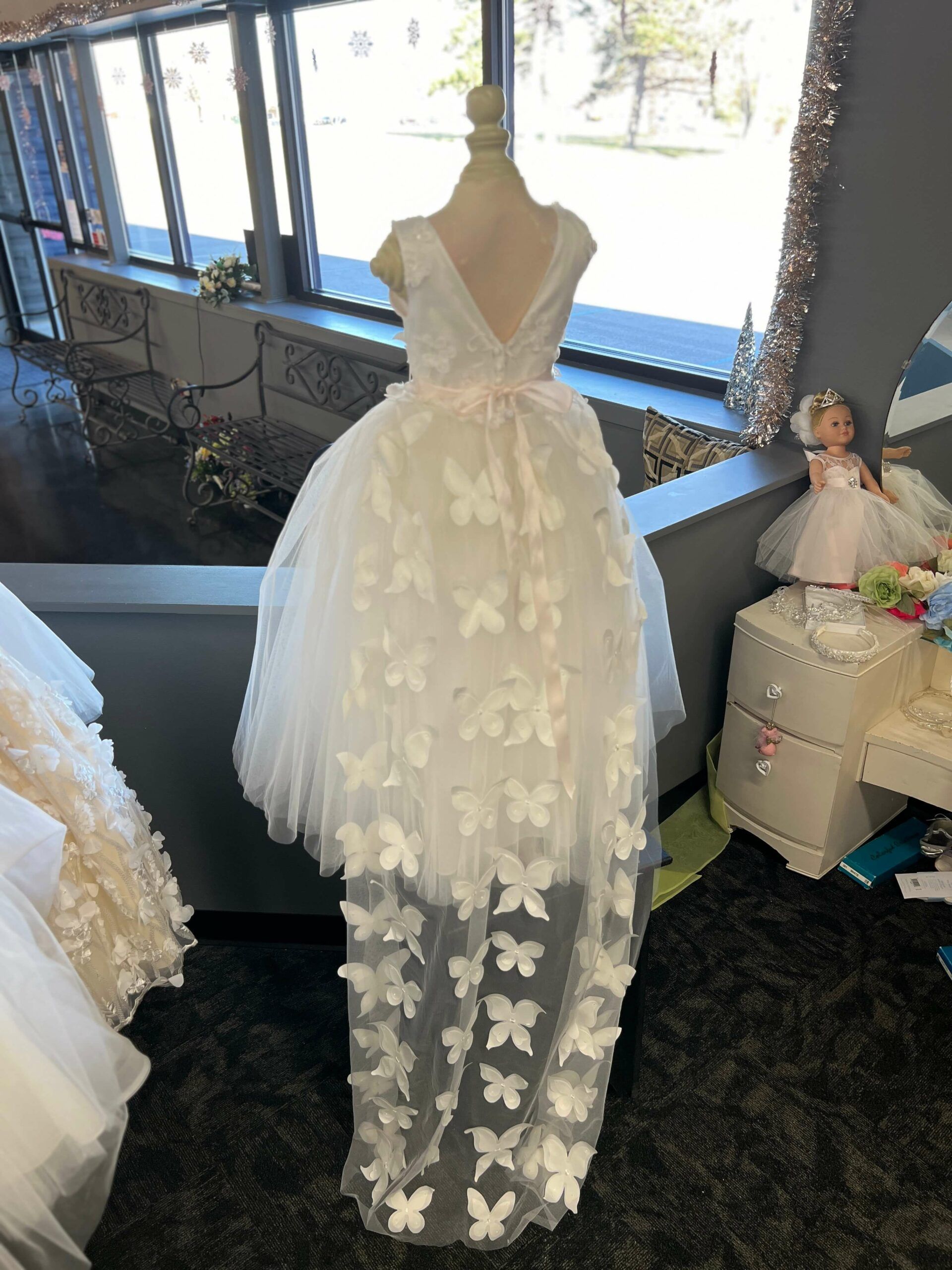 White dress with butterfly appliqués on a mannequin, in a shop window.