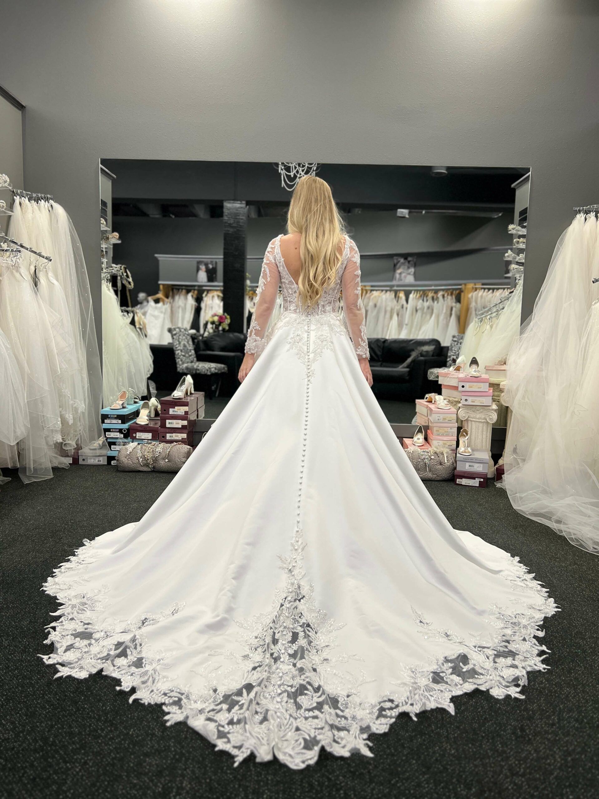 Bride in a white wedding dress with a long train, standing in a bridal shop.
