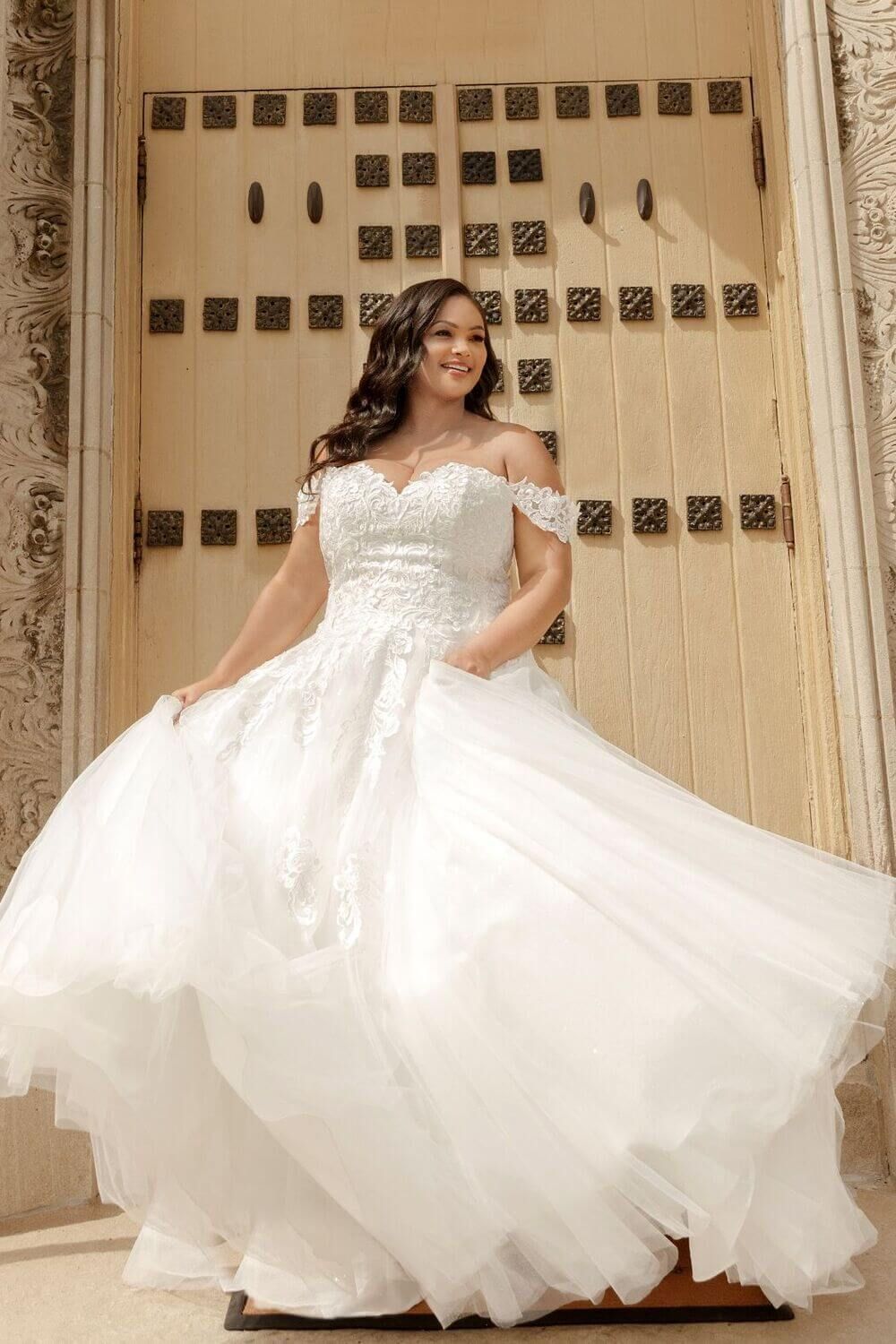 Woman in a white off-shoulder gown, posing in front of a light-colored wooden door.