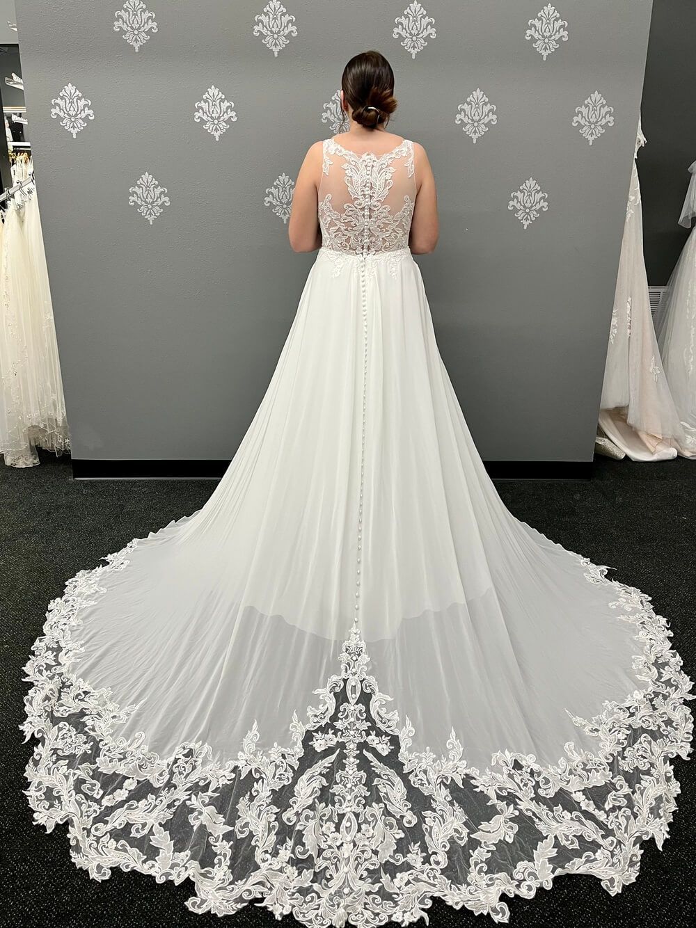Woman in a white wedding dress with lace detail, standing in a bridal shop.