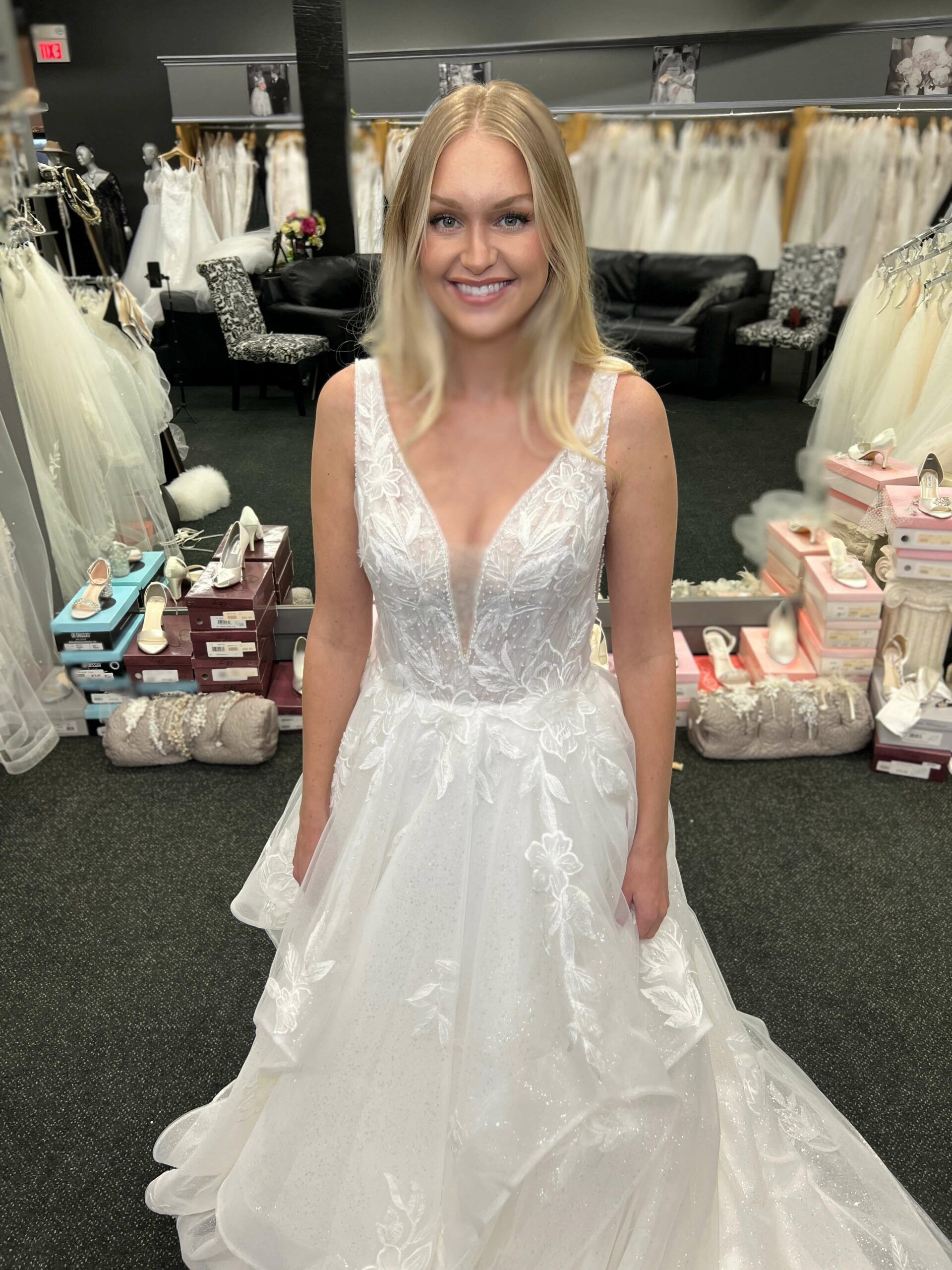 Blonde woman in a white wedding dress smiles in a bridal shop.