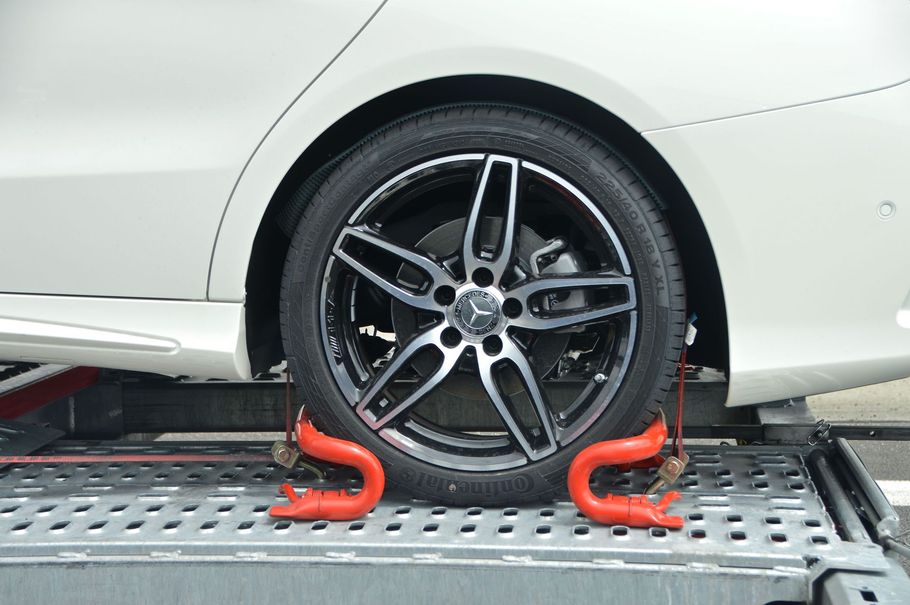 White car wheel secured with red clamps on a transport trailer
