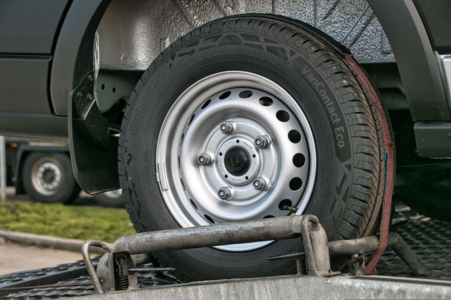 Flat tire on a silver car, with a damaged wheel resting on a curbside jack stand.