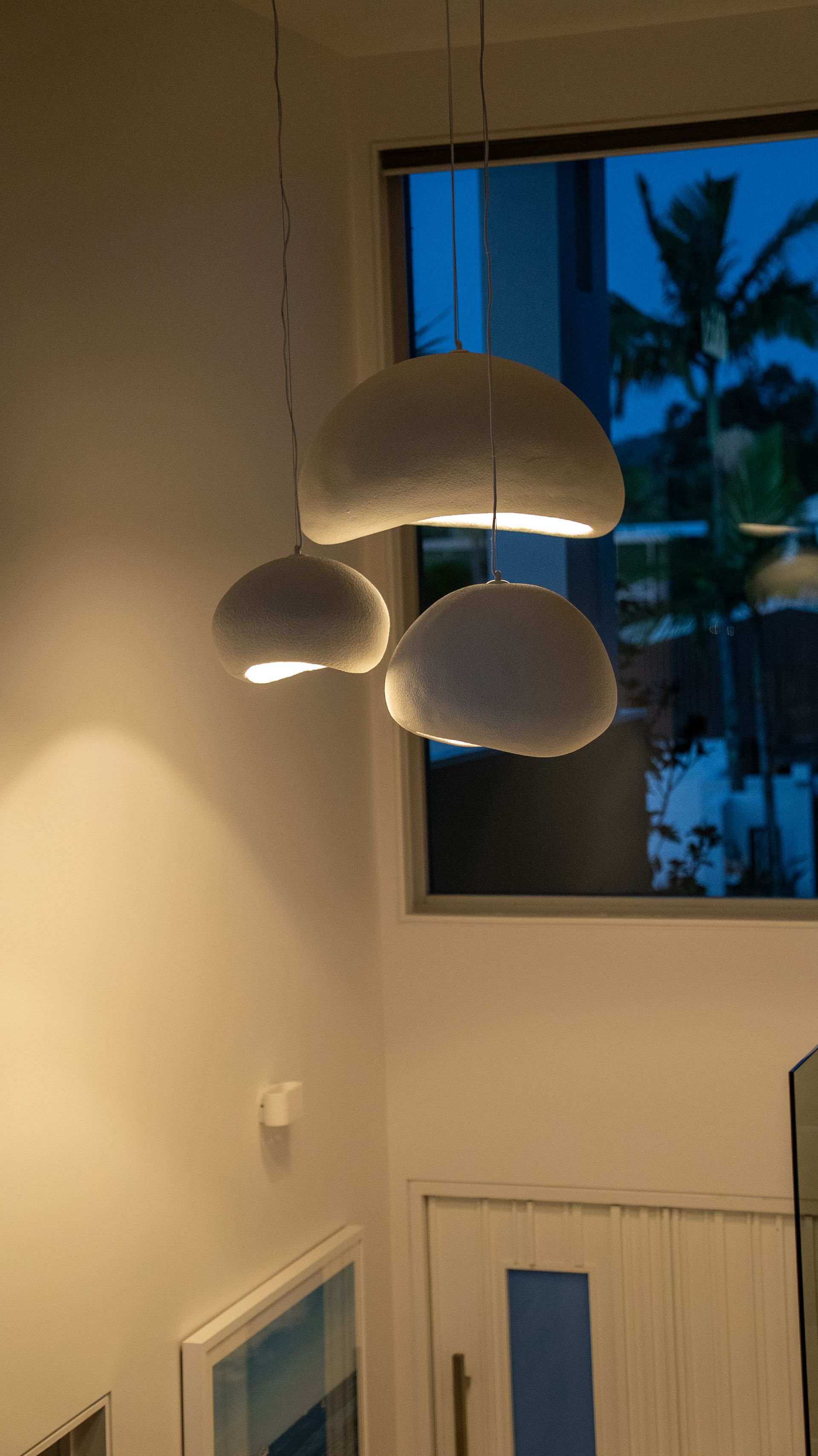 Modern Pendant Lights Hanging in A Warm-Lit Room by A Window with Palm Trees Outside — Ralph Ottmann Electrical in Pomona, QLD
