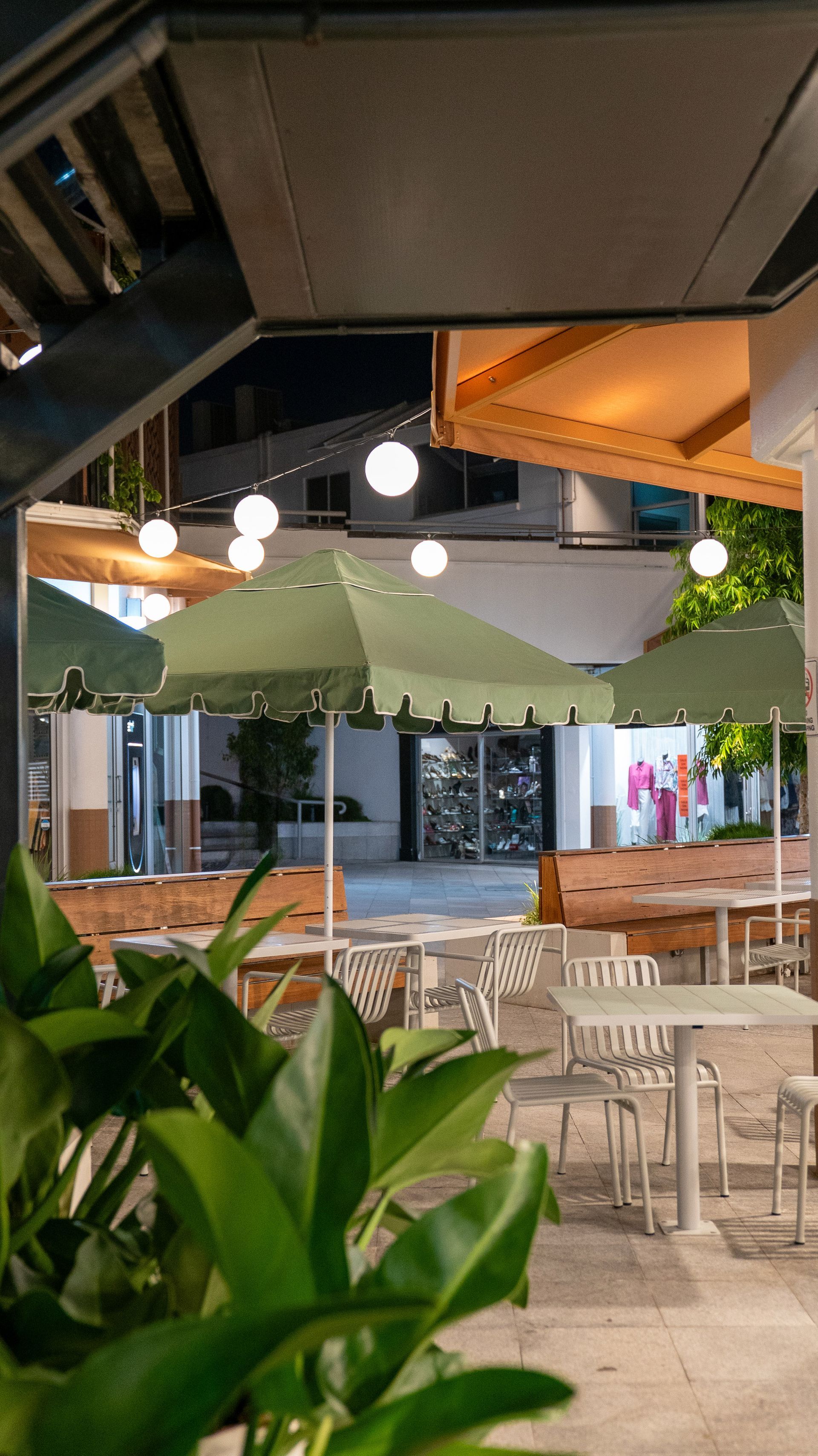 Outdoor Café Patio with White Tables and Chairs, Hanging Lights, and Green Plants Under an Awning — Ralph Ottmann Electrical in Pomona, QLD