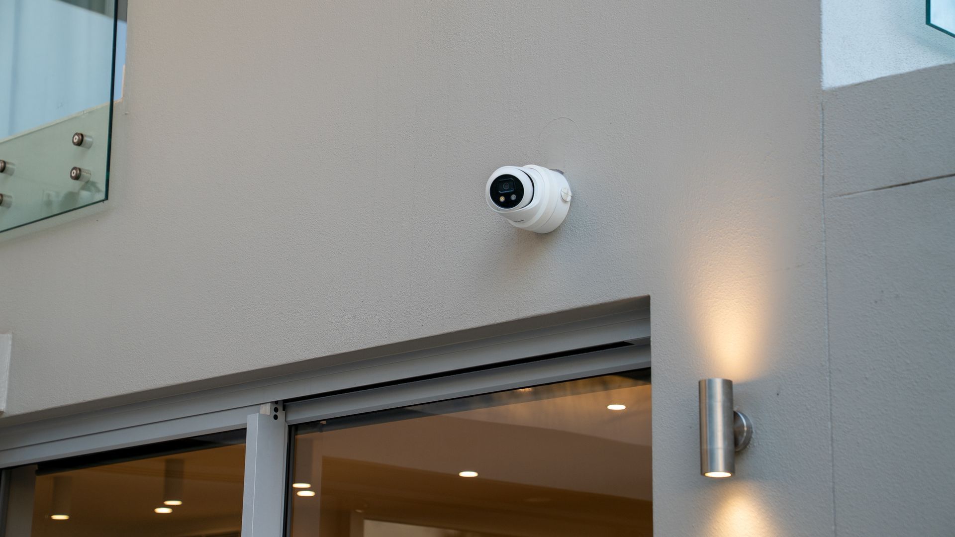 White Security Camera Mounted on An Exterior Wall Above a Storefront Entrance — Ralph Ottmann Electrical in Pomona, QLD