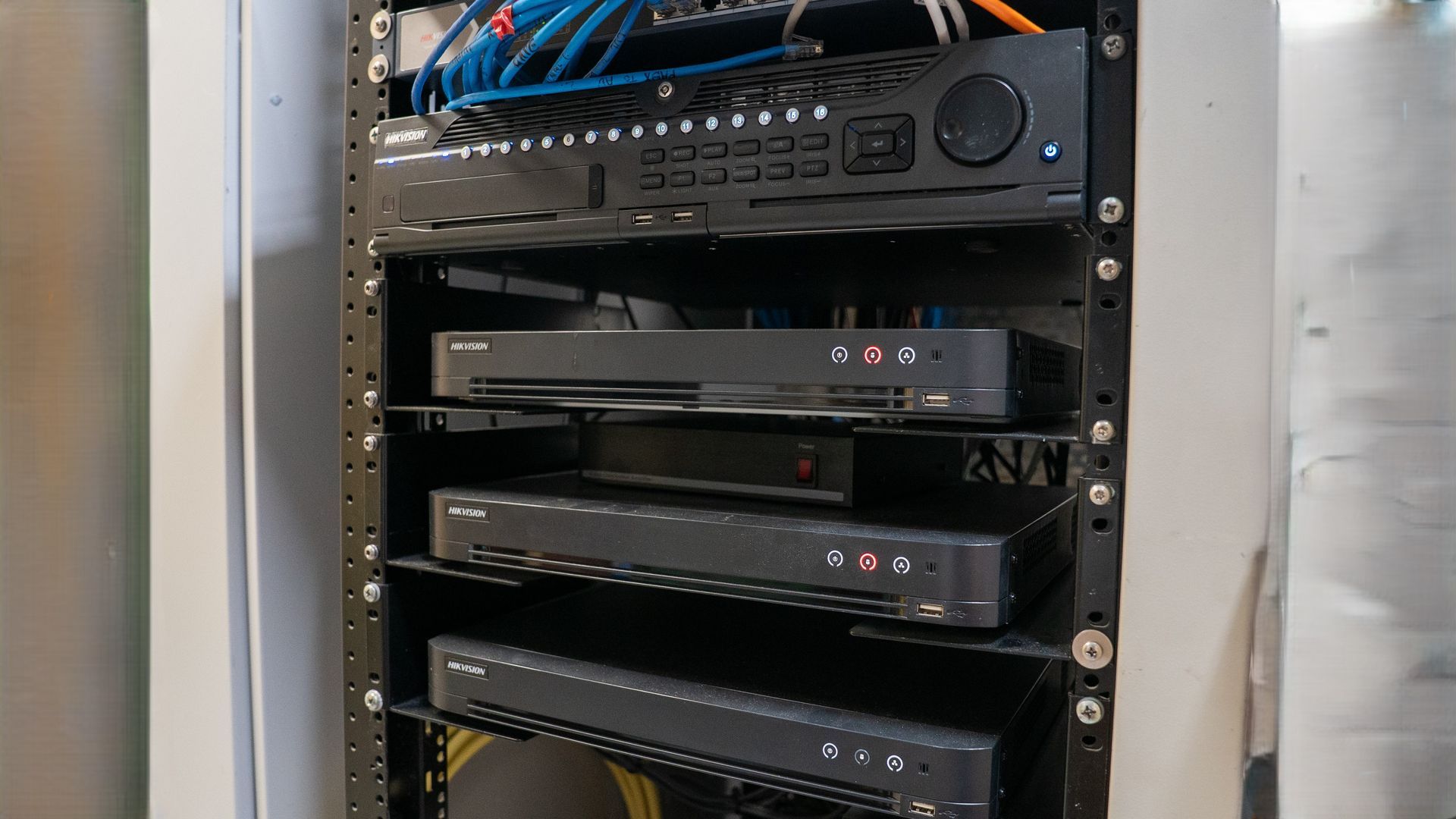 Server rack with stacked black networking equipment and blue cables in a data closet — Ralph Ottmann Electrical in Pomona, QLD