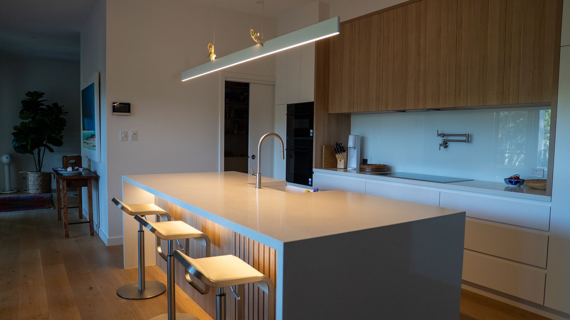 Modern Kitchen With Large Island, Pendant Light, Bar Stools, and Wood Cabinetry — Ralph Ottmann Electrical in Tewantin, QLD