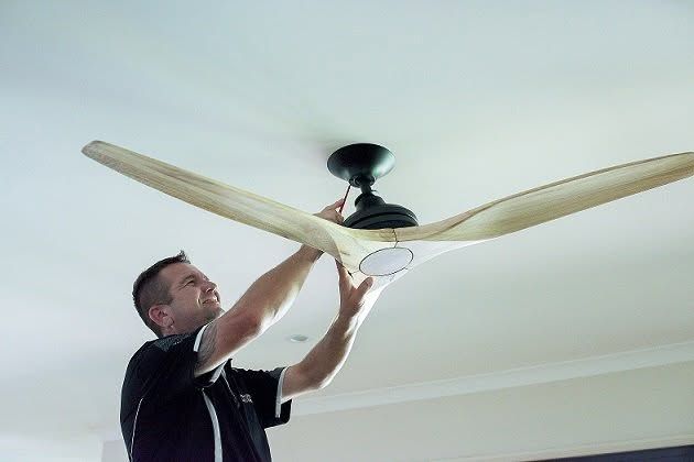 Man Adjusting a Ceiling Fan with A Ladder in A Bright Room — Ralph Ottmann Electrical in Noosaville, QLD