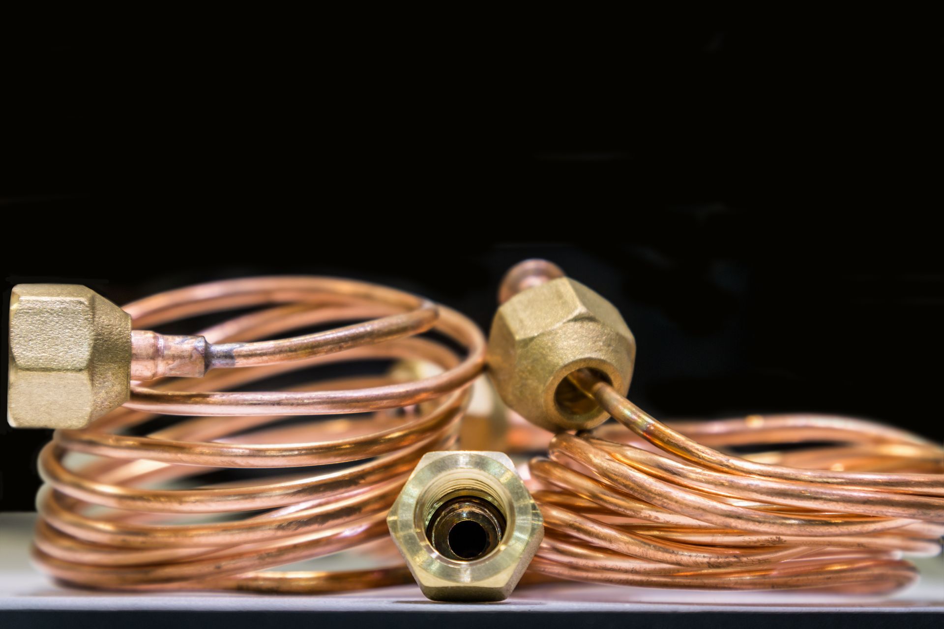 coiled copper tubing with brass fittings, arranged against a black background.