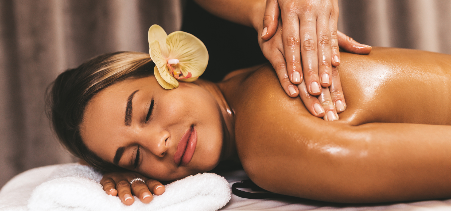 Woman receiving a spa massage with a yellow orchid in her hair, resting on a towel.
