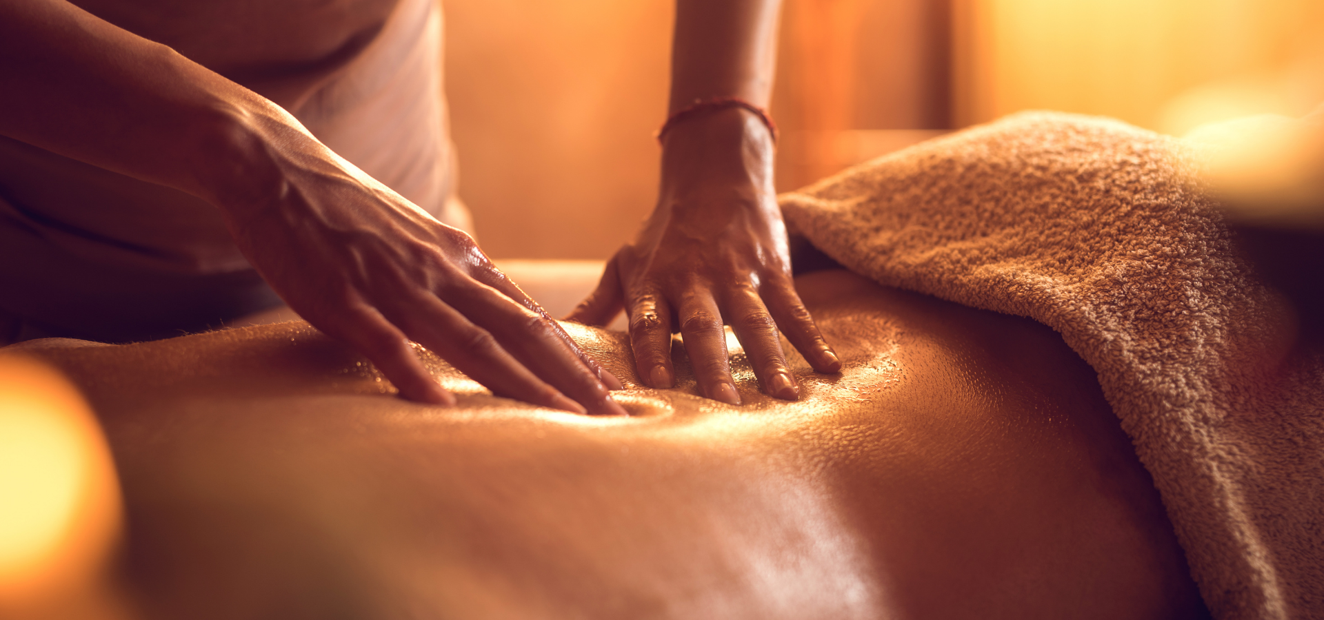Hands massaging a person's bare back with a warm towel in a spa setting