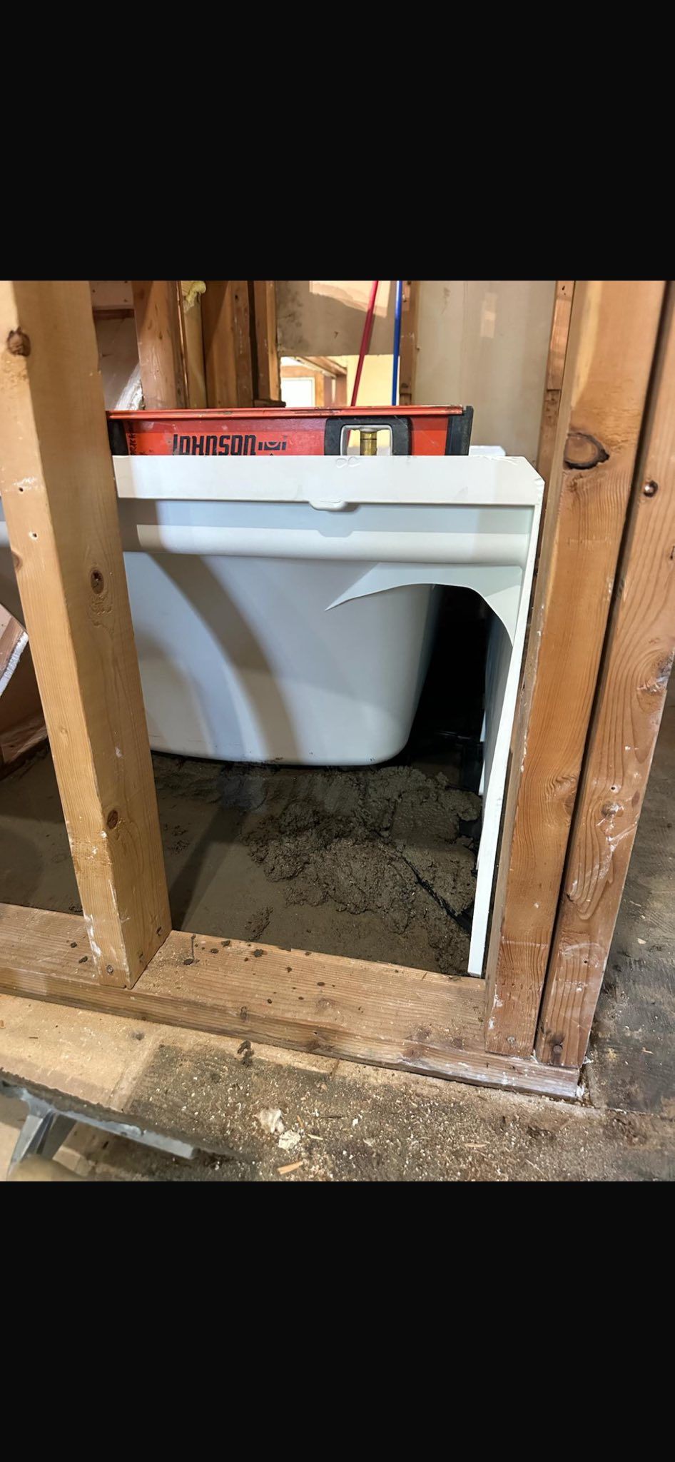 White toilet installed in a rough wooden-framed wall opening with exposed plumbing and construction debris
