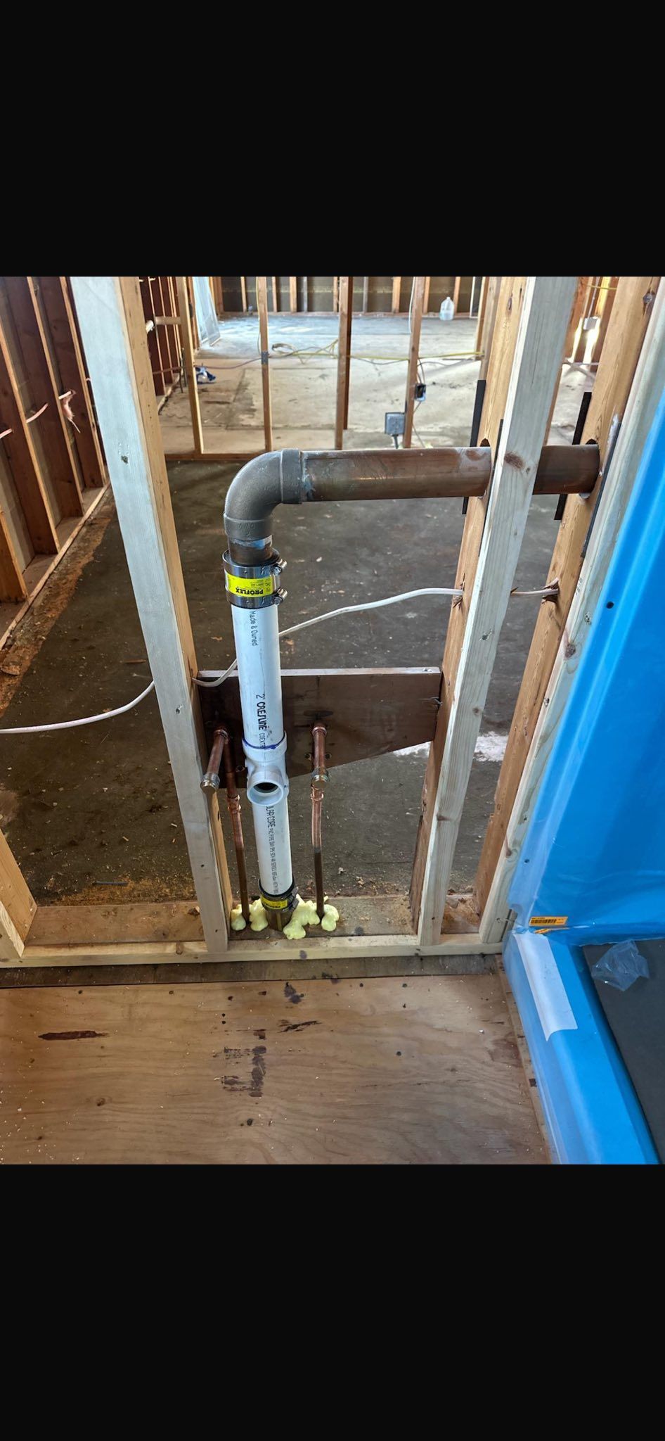 Open wall with exposed plumbing pipe and framing beside a blue door frame
