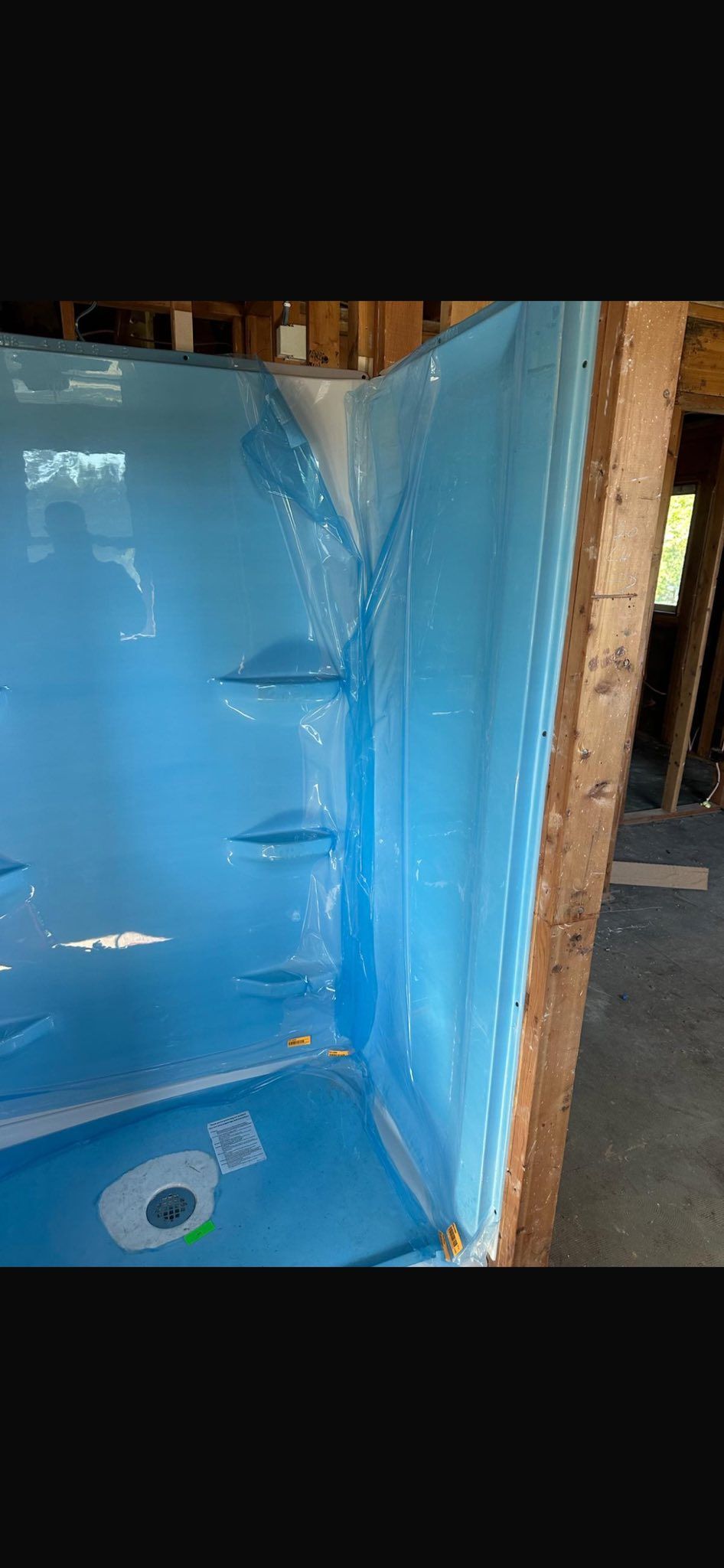 Blue-lined shower stall under construction with exposed framing and plumbing opening at the bottom