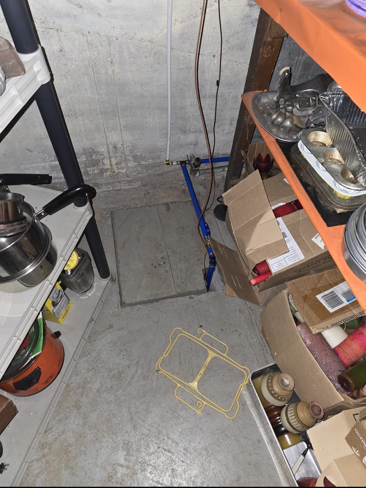 Narrow storage aisle with shelves, cardboard boxes, and hanging cables on a concrete floor.