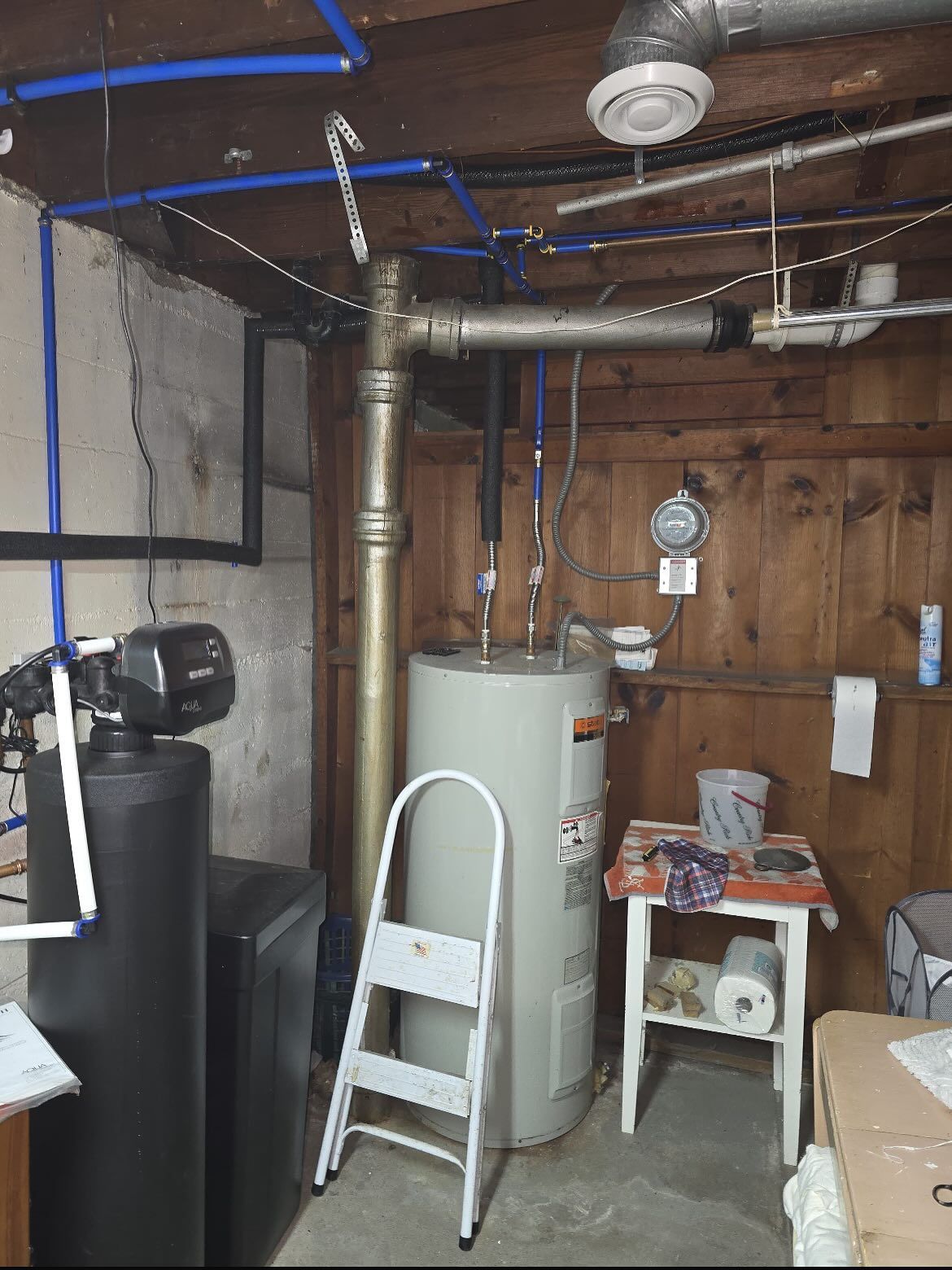 Basement utility room with water heater, exposed pipes, ladder, and wooden wall paneling
