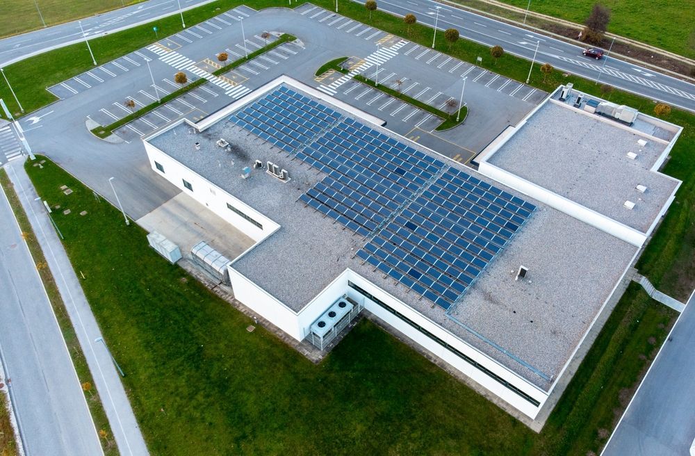 Aerial view of a building with a large rooftop solar panel array and surrounding parking lot.