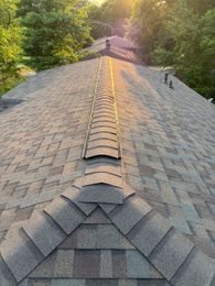 Two workers in hard hats installing roofing panels on a metal roof under a clear sky