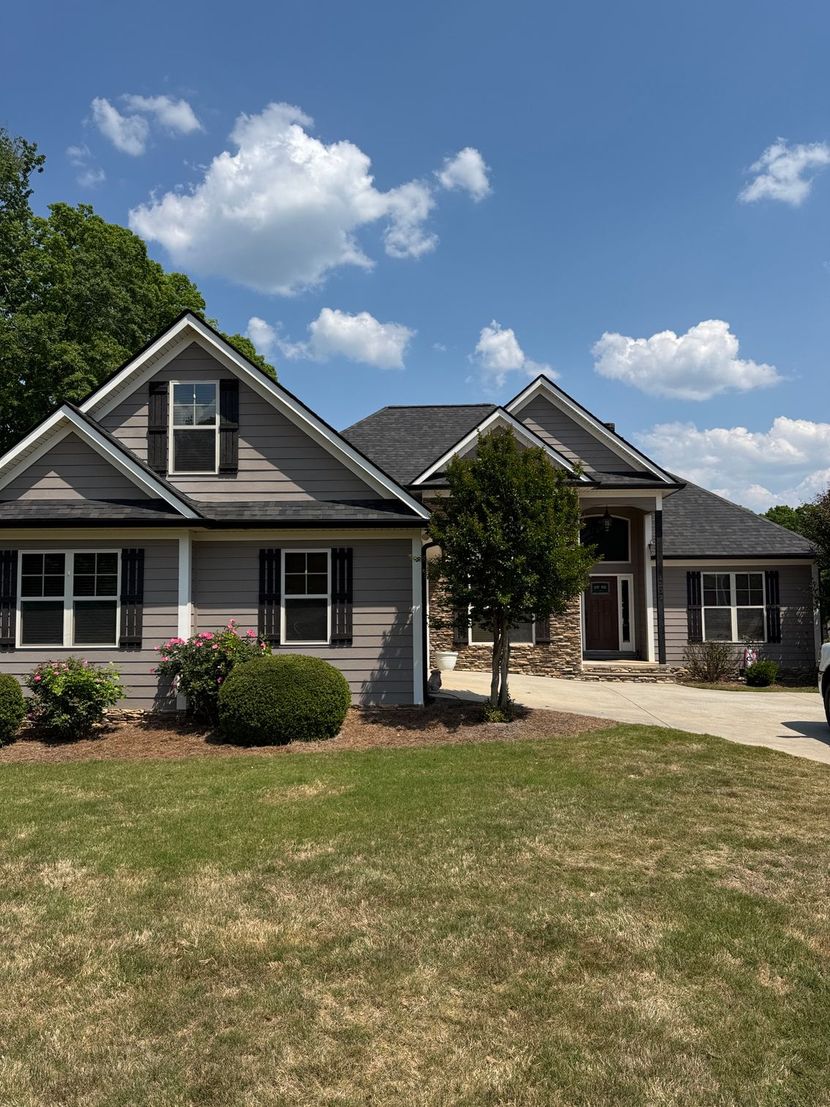 Suburban house with gray siding, black shutters, and a front lawn under a partly cloudy blue sky