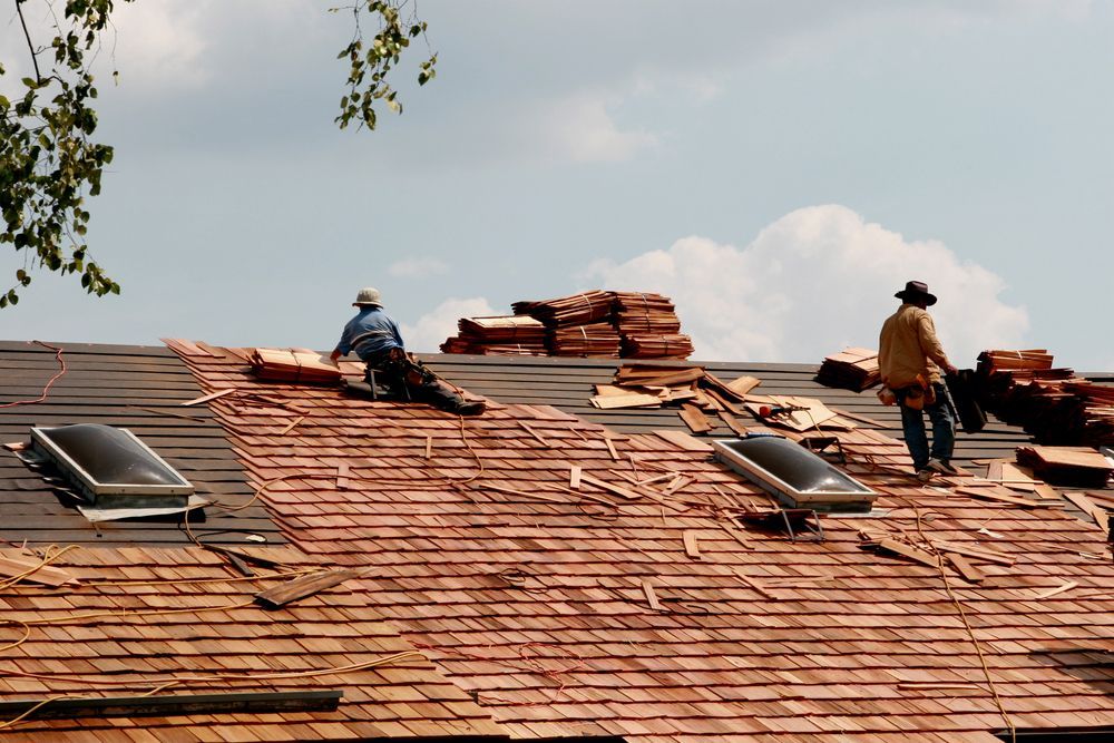 Workers repairing a shingled roof with skylights under a partly cloudy sky