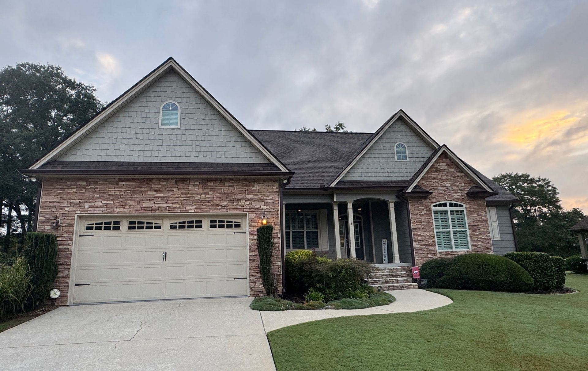 Suburban brick house with two-car garage, front porch, and neatly kept lawn at dusk