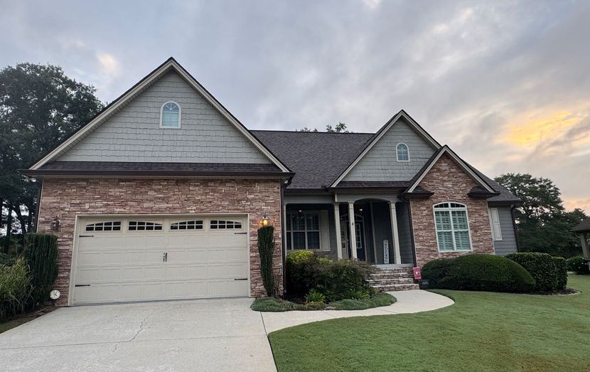 Suburban brick house with two-car garage, front porch, and neatly kept lawn at dusk