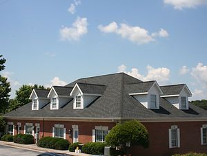 Brick building with gray shingle roof and white dormer windows under a blue sky